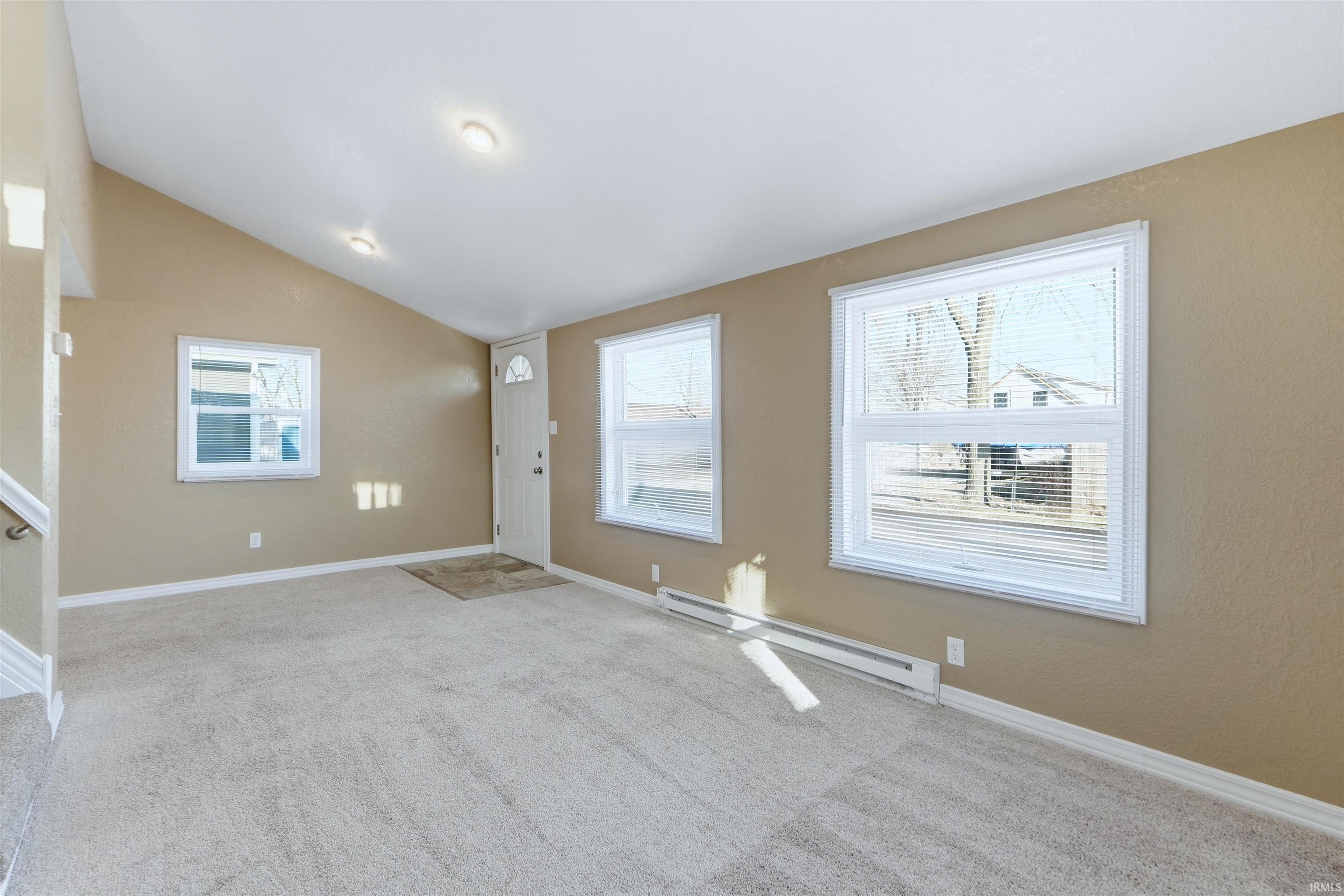 Unfurnished living room featuring a baseboard radiator, light carpet, and vaulted ceiling