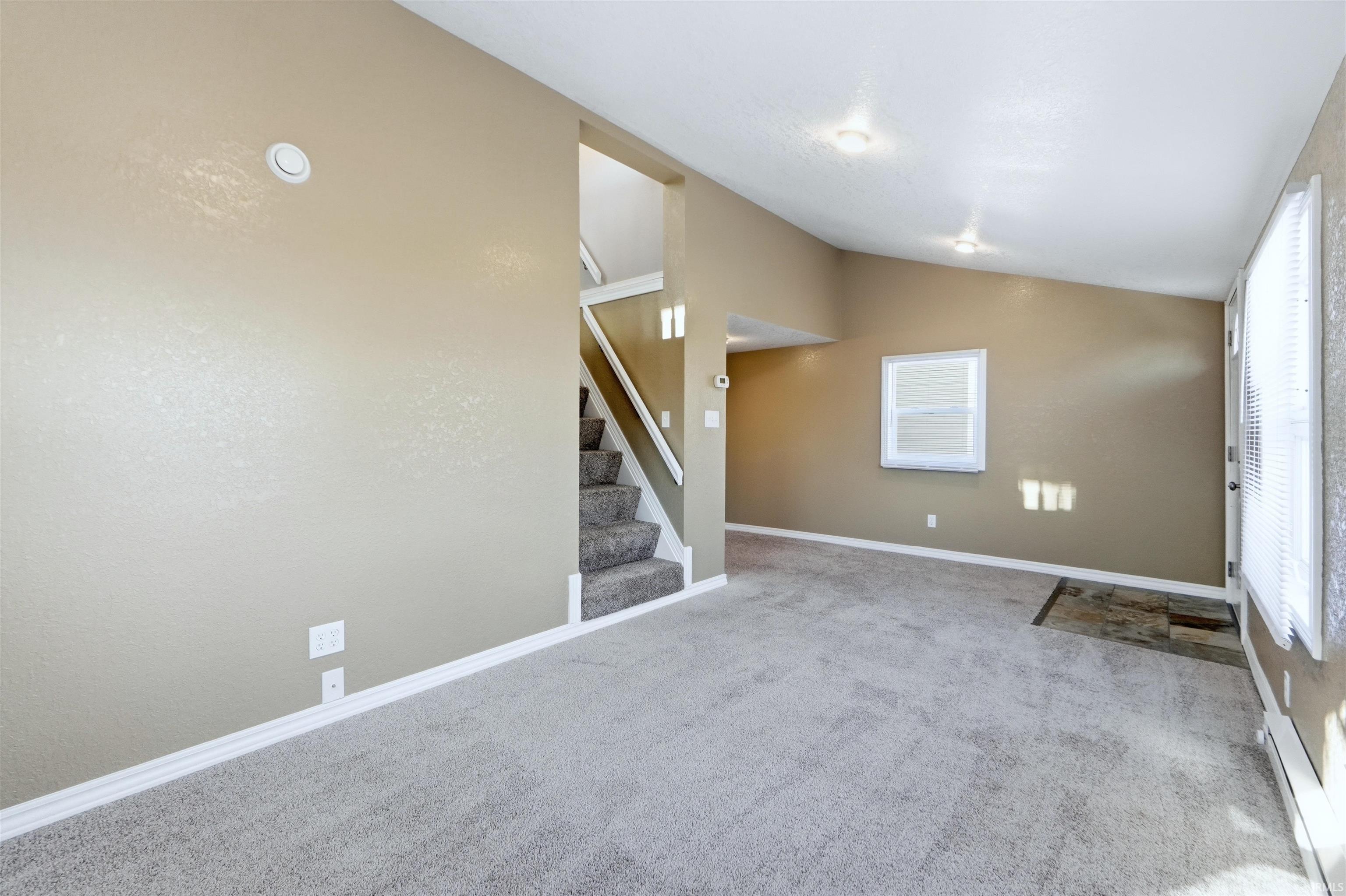Unfurnished living room with light carpet, baseboard heating, and lofted ceiling