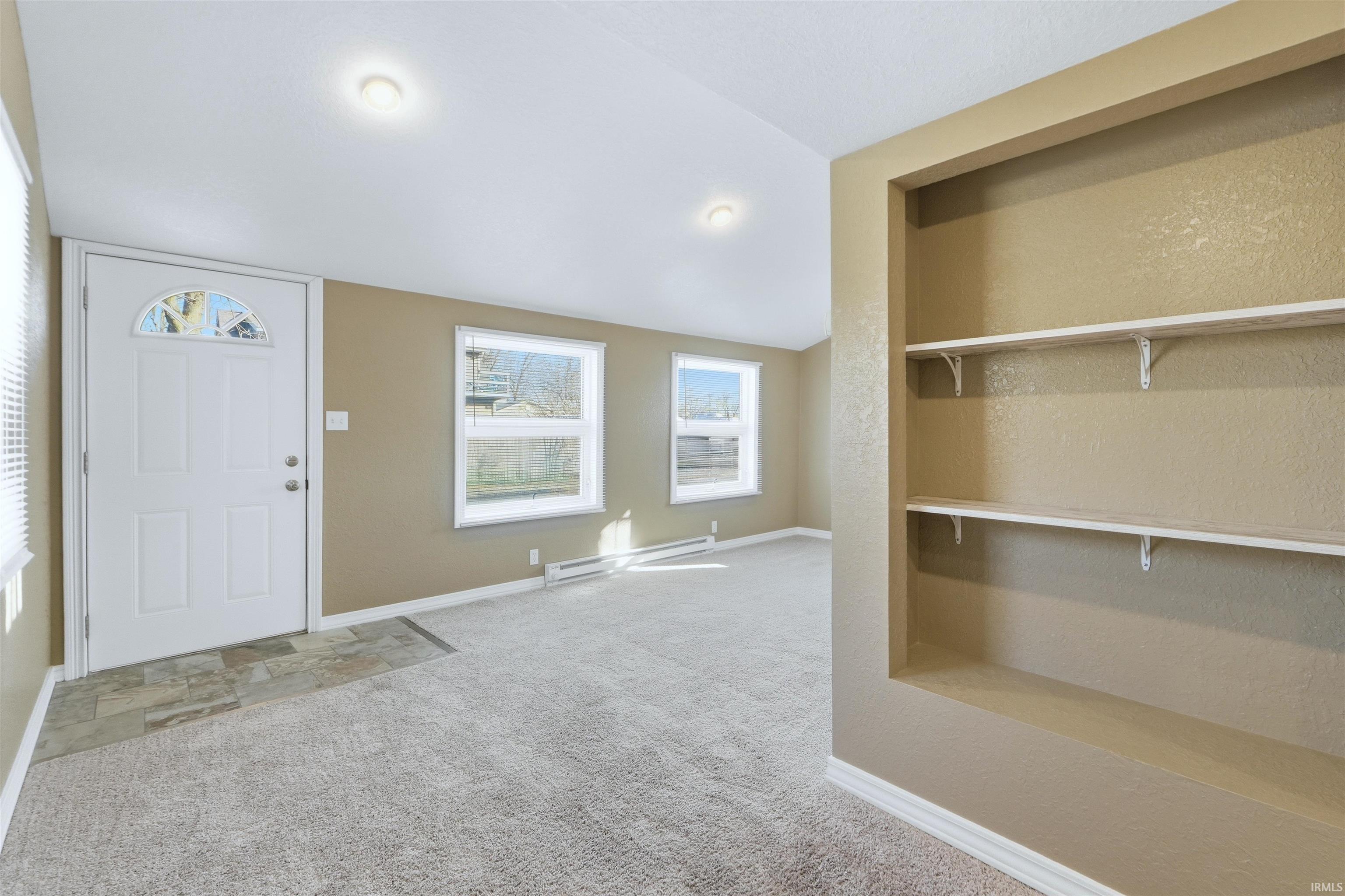 Foyer entrance with carpet floors, a baseboard heating unit, vaulted ceiling, and a textured wall