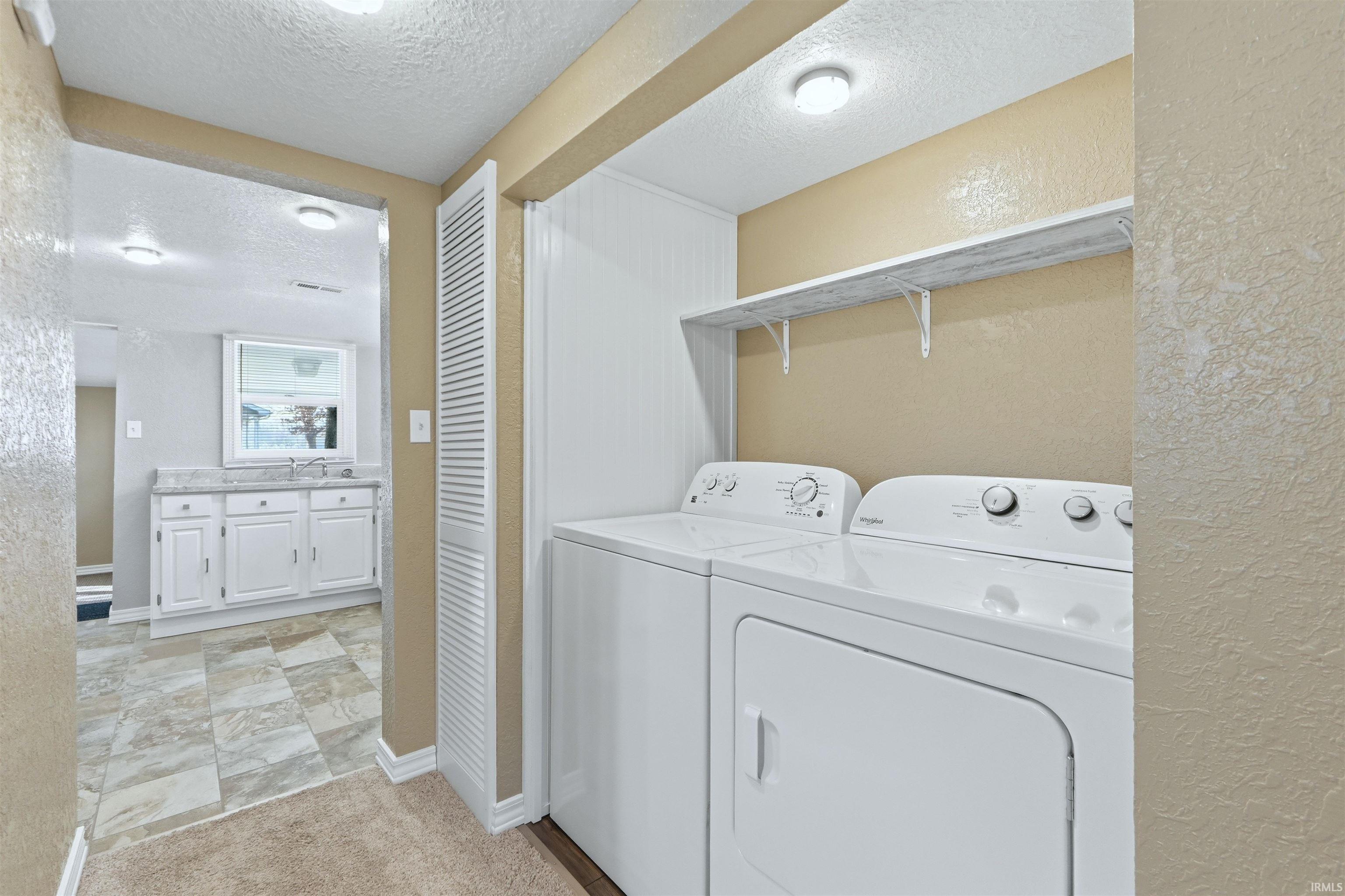 Laundry area with a textured wall, a textured ceiling, and independent washer and dryer