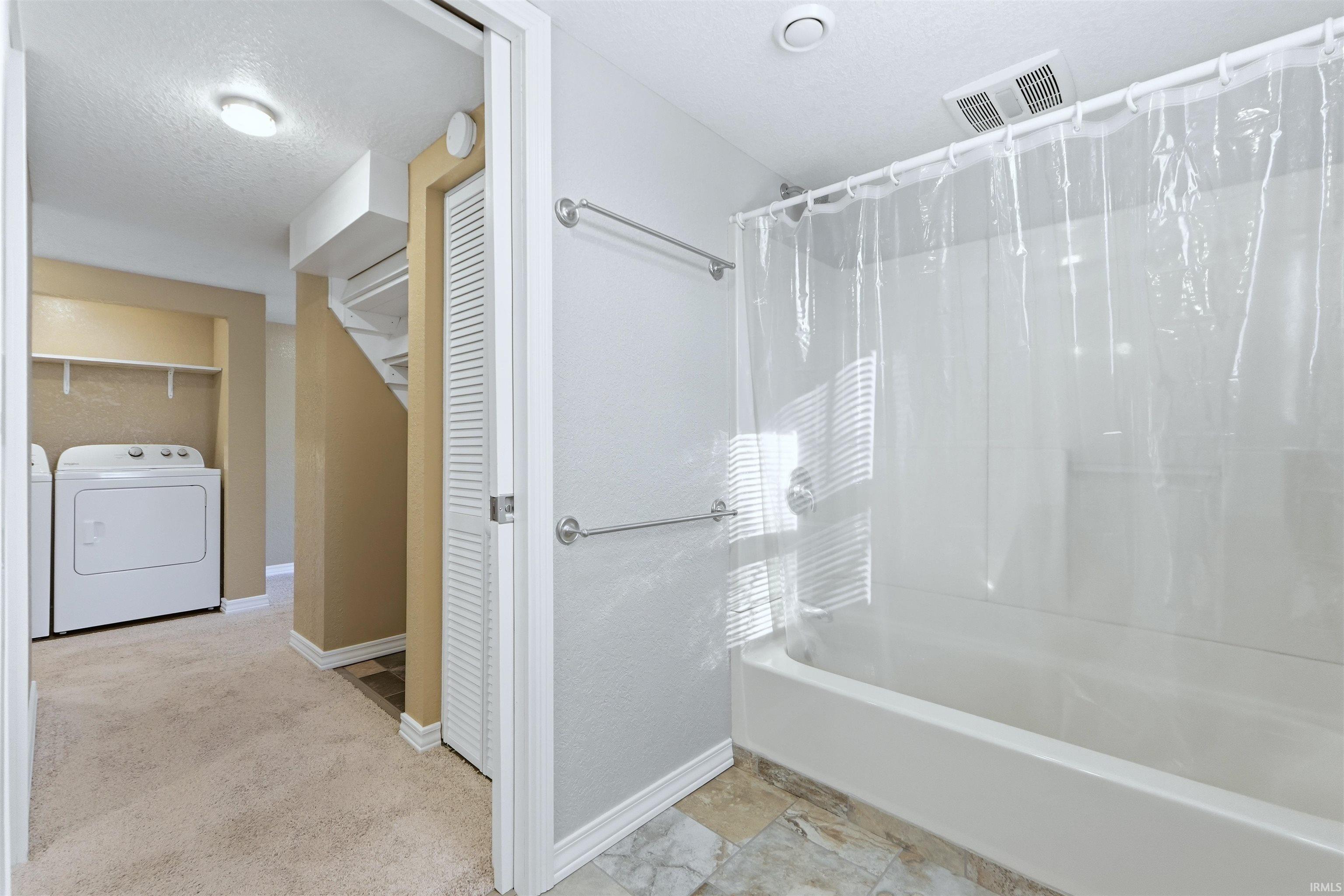 Bathroom featuring a closet, shower / bath combination with curtain, independent washer and dryer, a textured ceiling, and light colored carpet