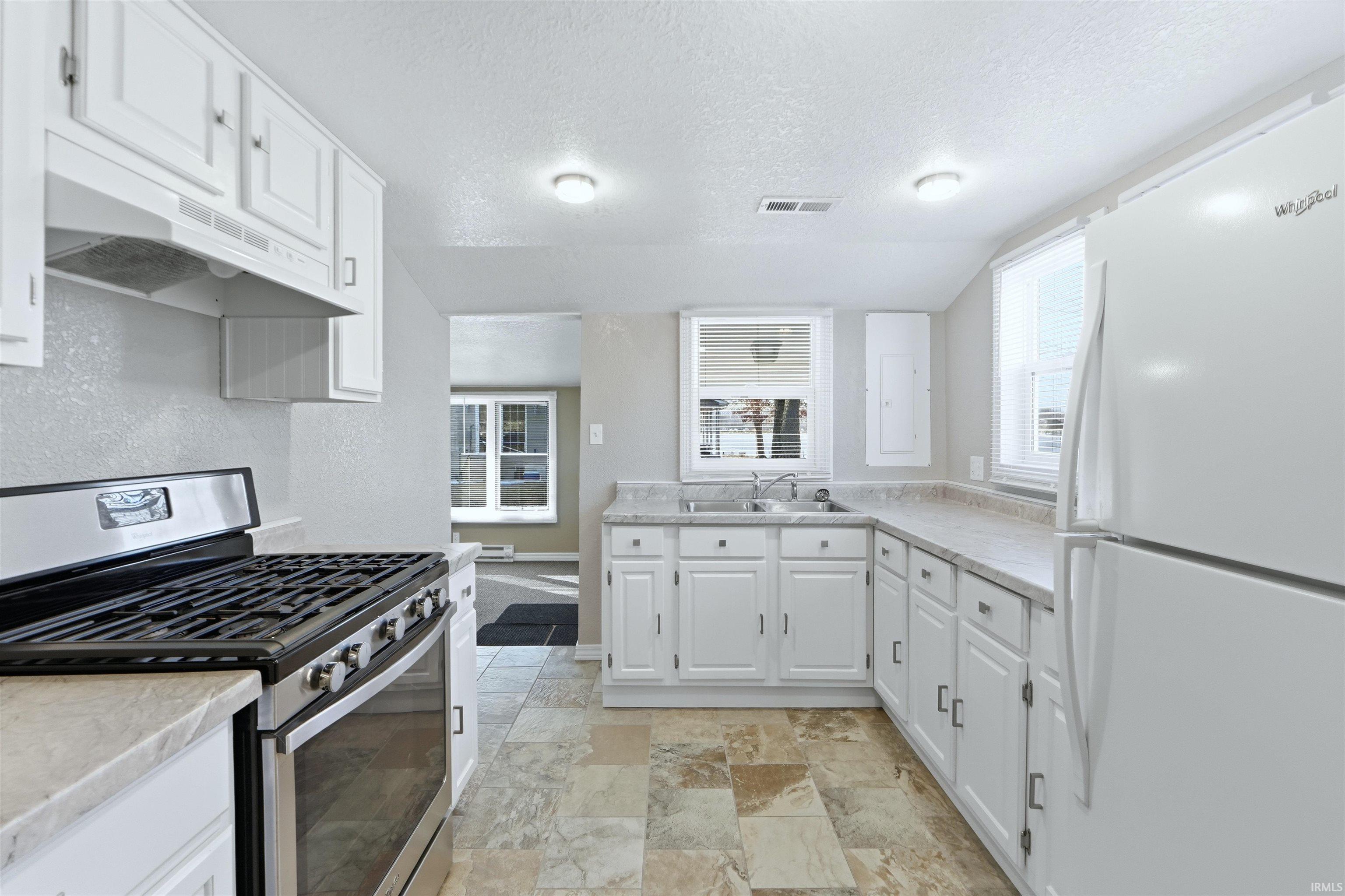 Kitchen featuring stainless steel range with gas cooktop, white cabinets, freestanding refrigerator, light countertops, and a textured ceiling