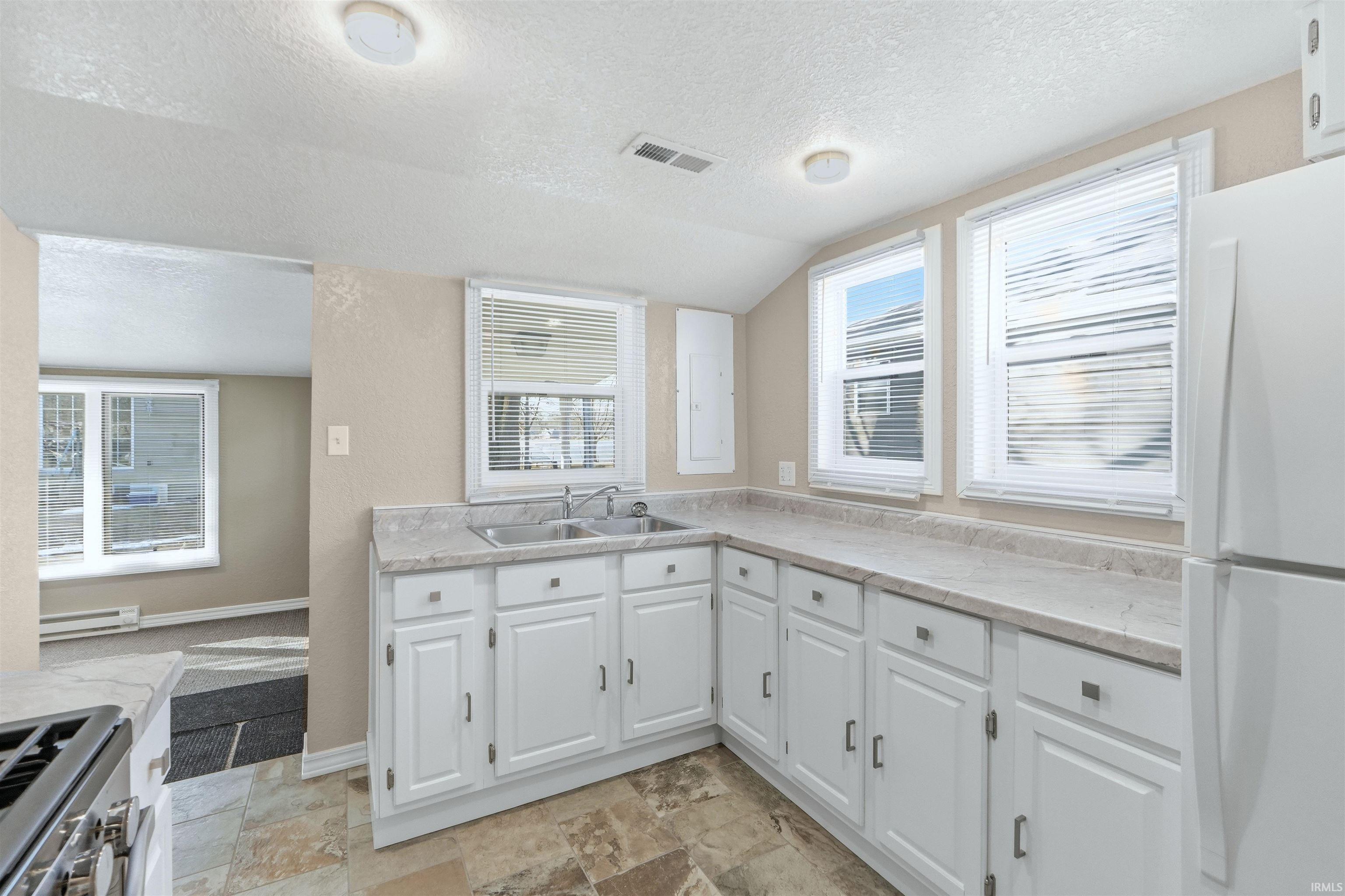 Kitchen featuring freestanding refrigerator, light countertops, gas stove, light stone finish floors, and a textured wall