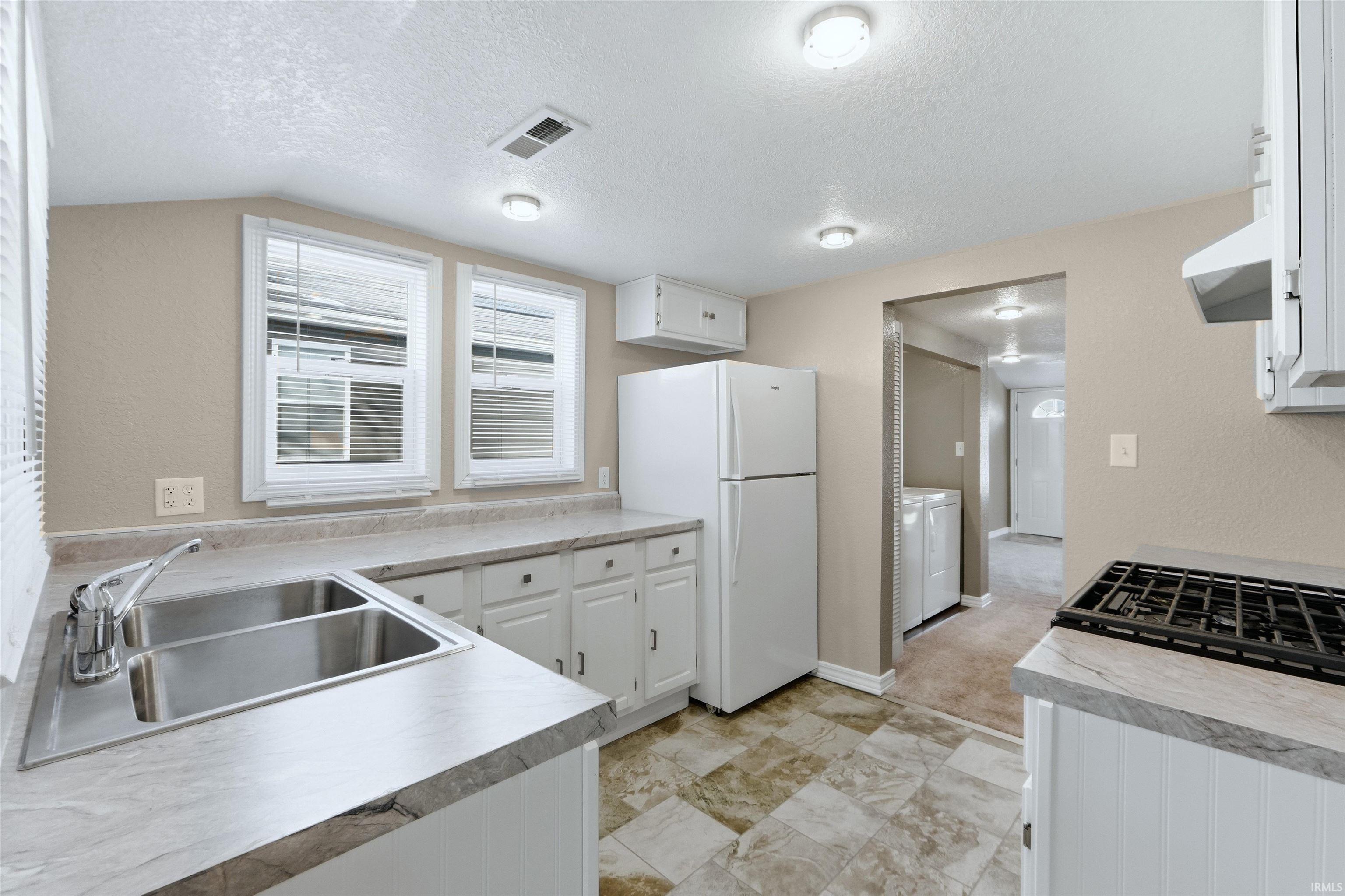 Kitchen with white cabinetry, freestanding refrigerator, a textured wall, light countertops, and a textured ceiling