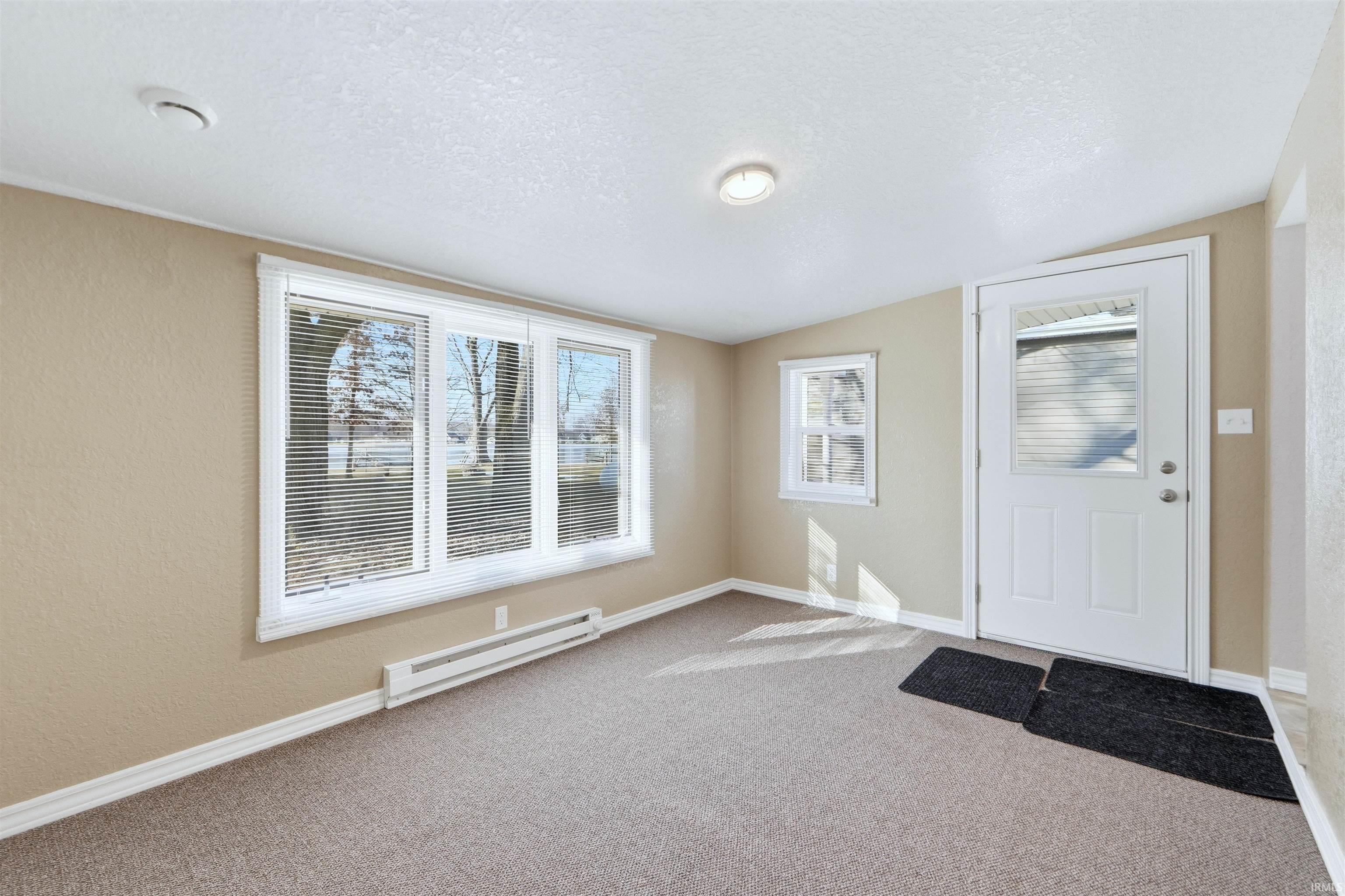 Entrance foyer with baseboard heating, light colored carpet, and a textured wall