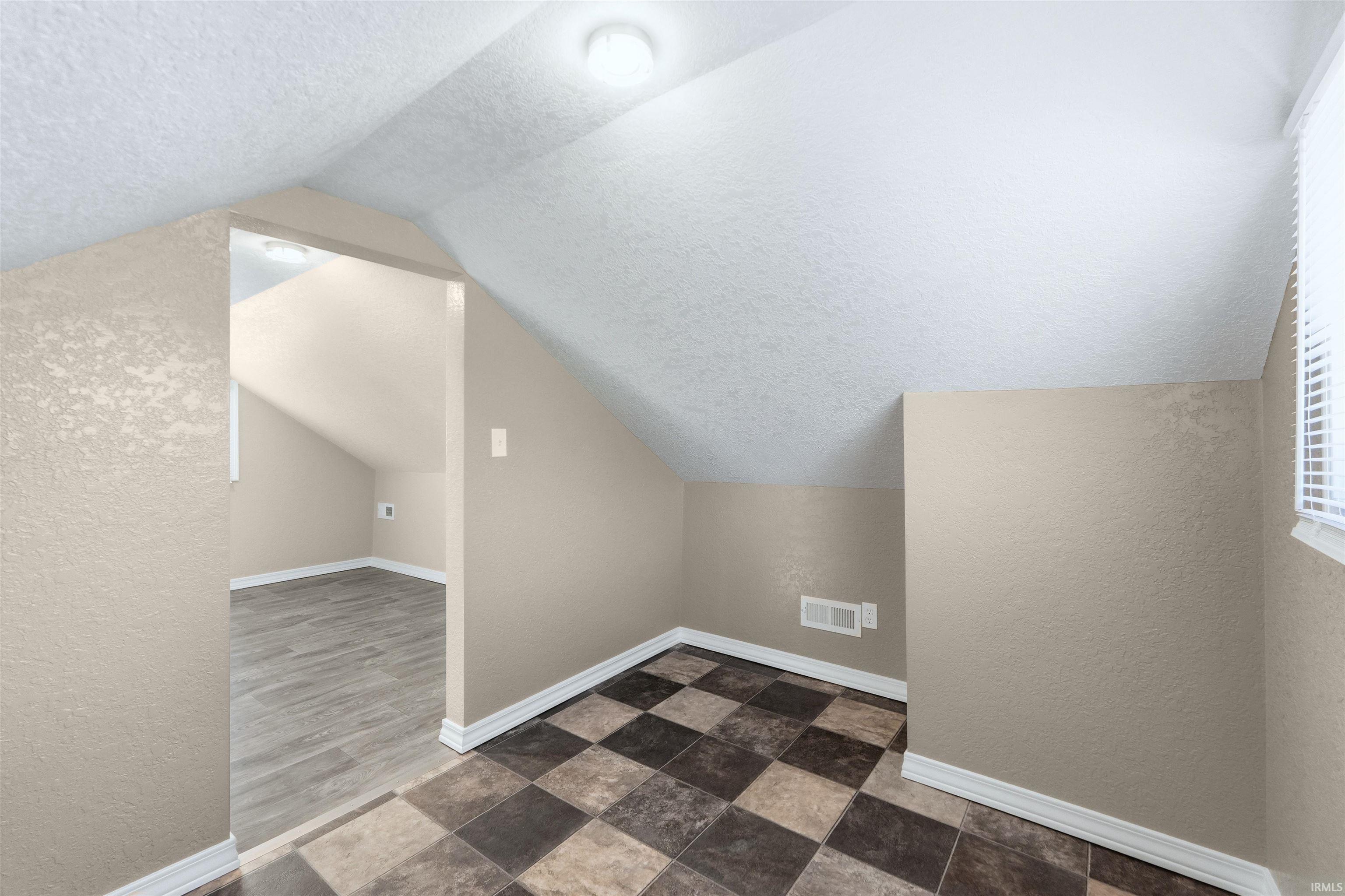 Additional living space with a textured wall and dark stone finish floors