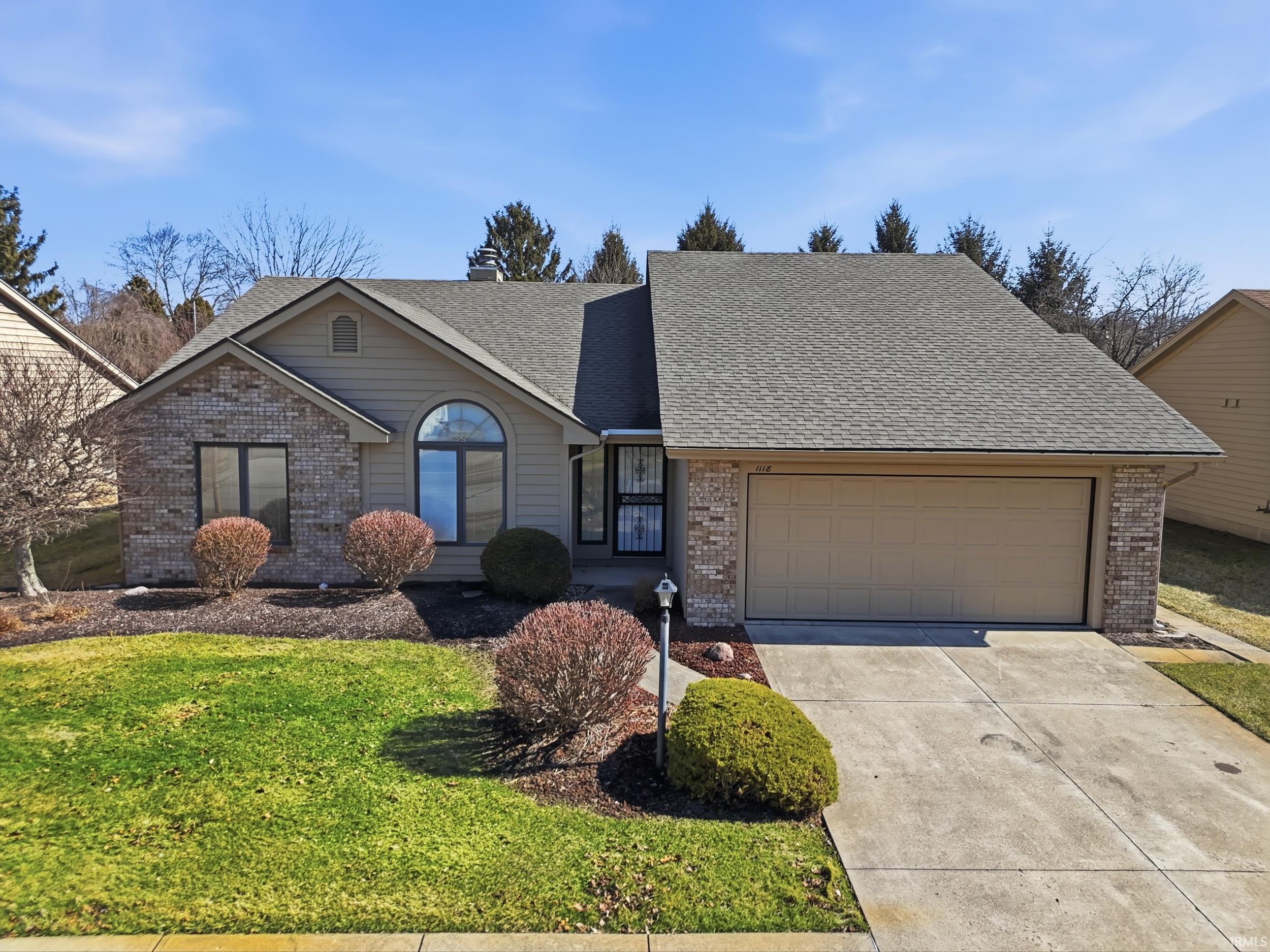 View of front of home with brick siding, roof with shingles, concrete driveway, and a front yard