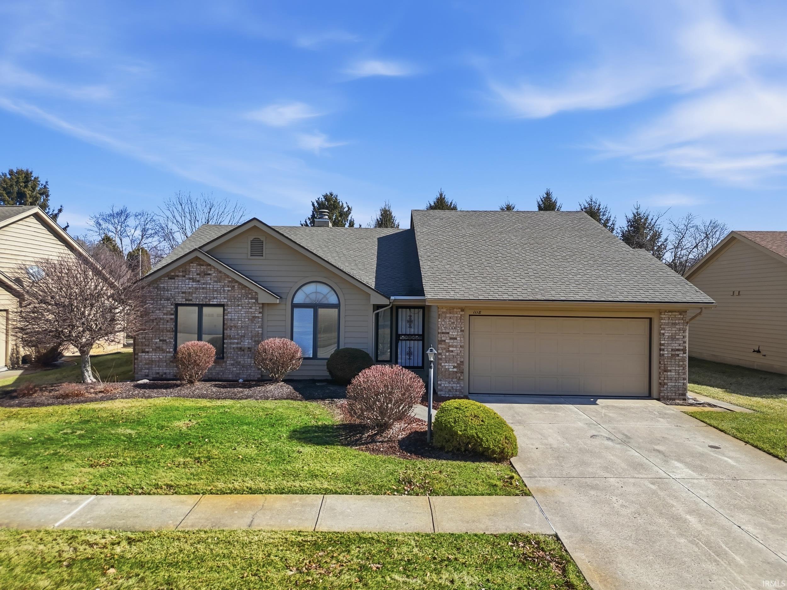 Single story home with brick siding, a shingled roof, an attached garage, and concrete driveway