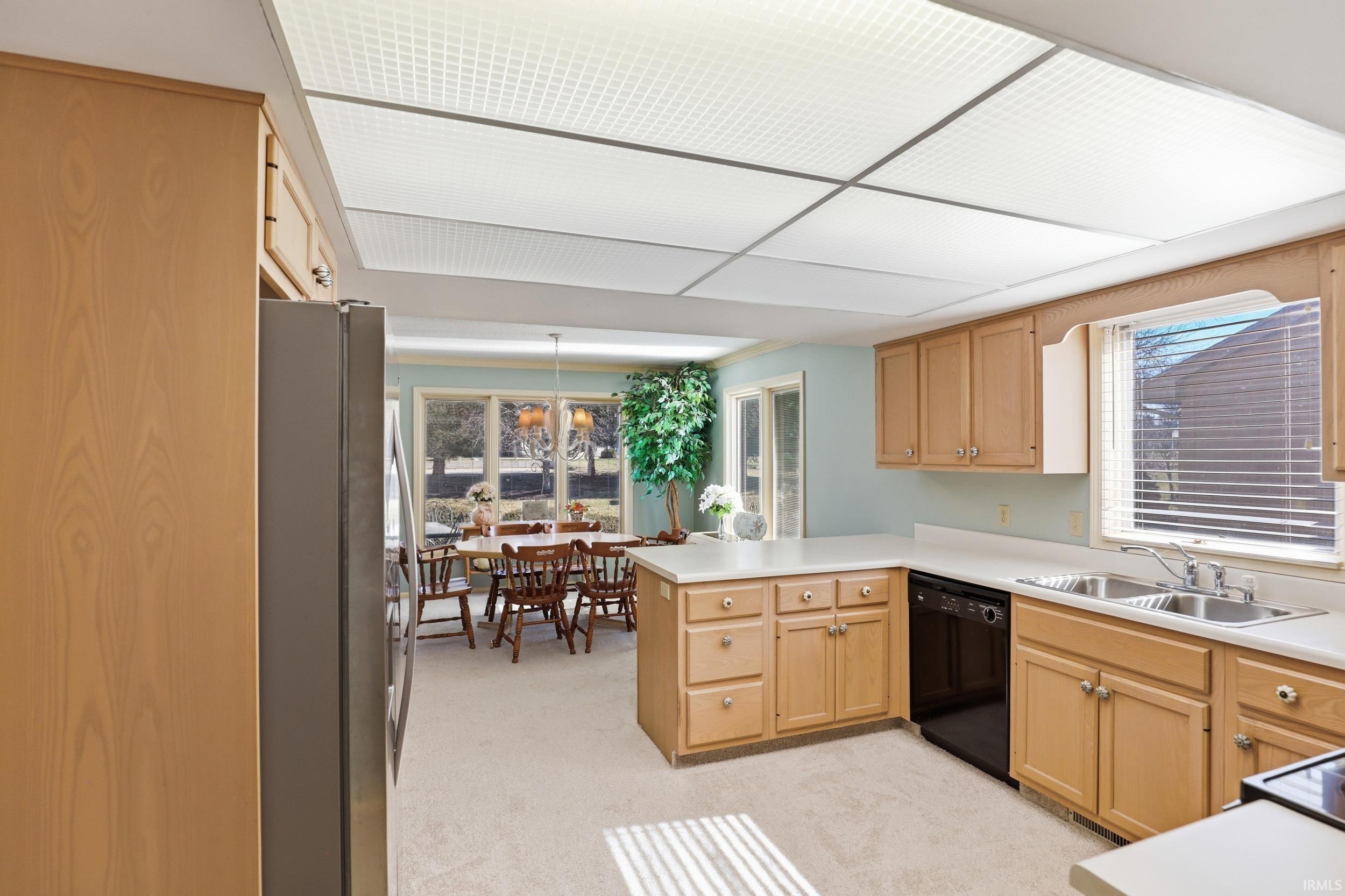 Kitchen with a peninsula, freestanding refrigerator, light countertops, black dishwasher, and light wood finish cabinetry