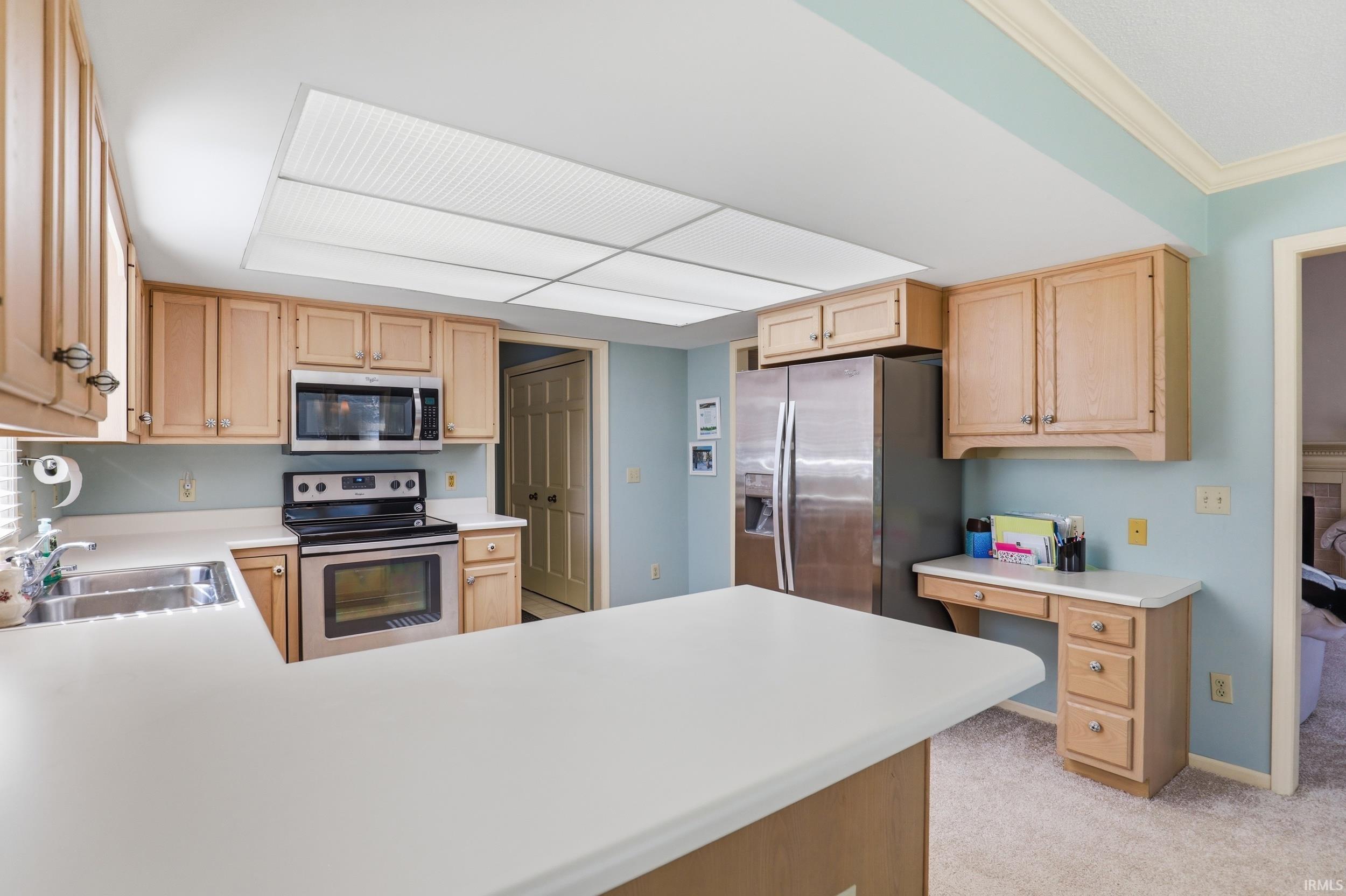 Kitchen featuring a peninsula, stainless steel appliances, light countertops, light carpet, and light wood finish cabinetry