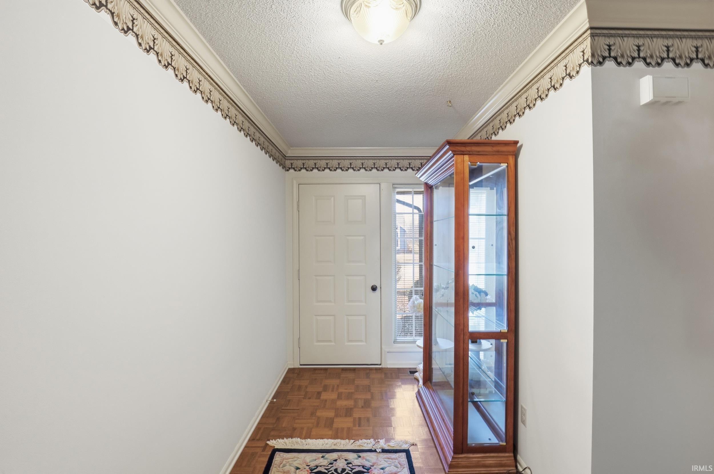 Entryway featuring a textured ceiling, parquet flooring, and ornamental molding