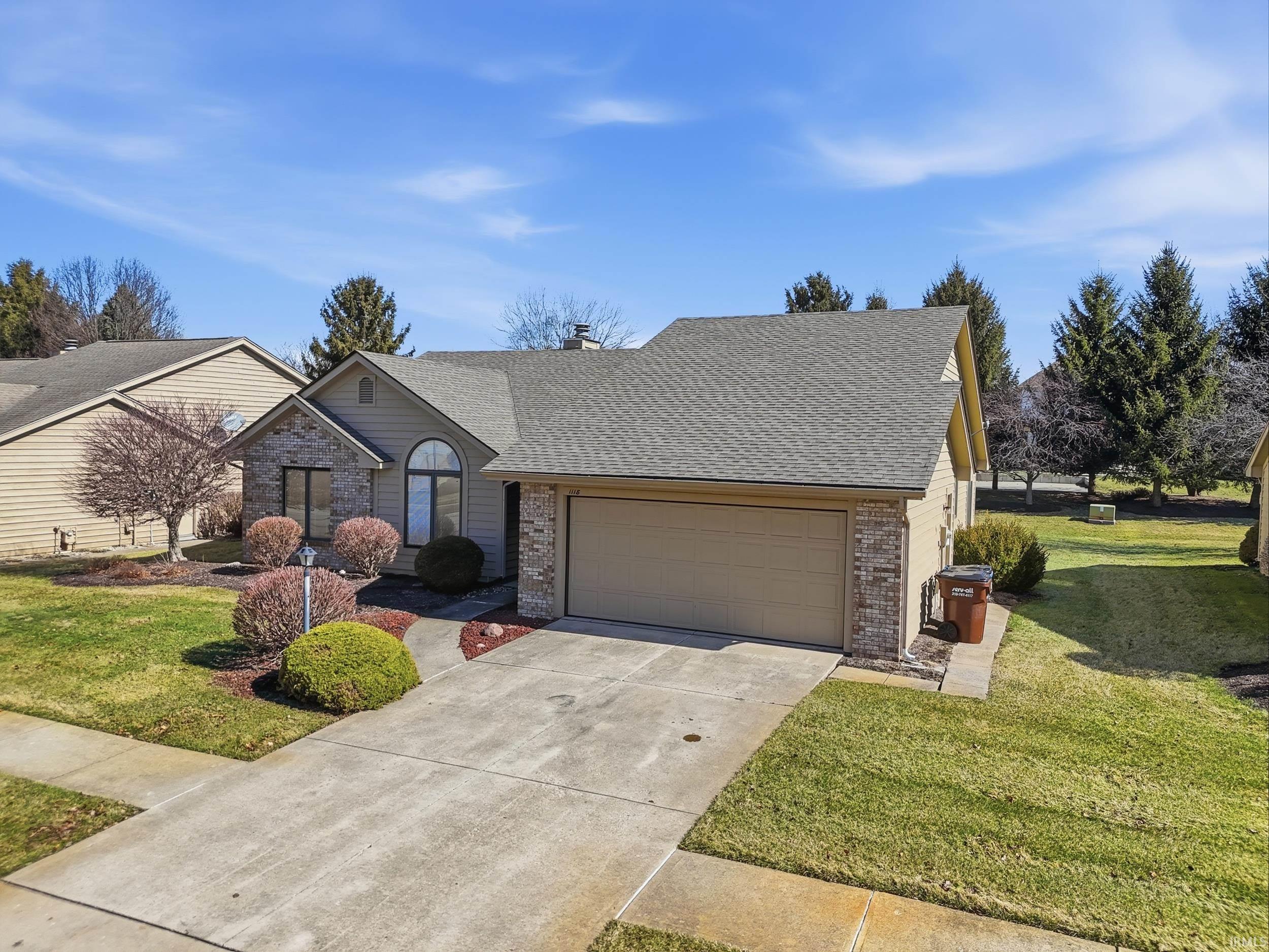 Traditional-style home featuring brick siding, an attached garage, a front lawn, and roof with shingles