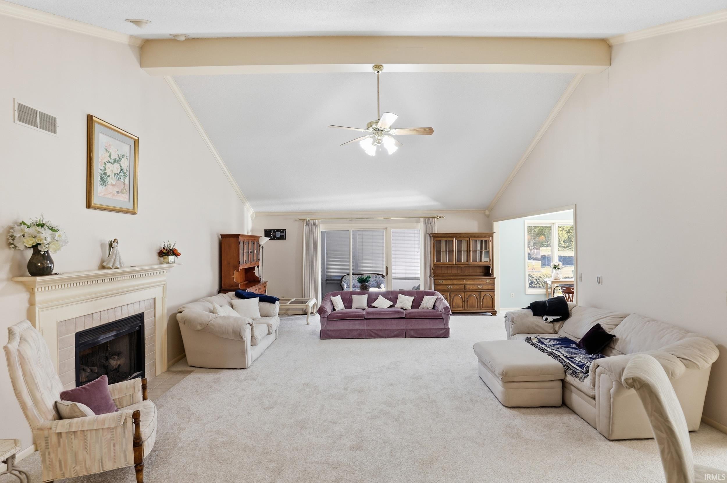 Living area with carpet floors, ceiling fan, a tiled fireplace, lofted ceiling, and crown molding