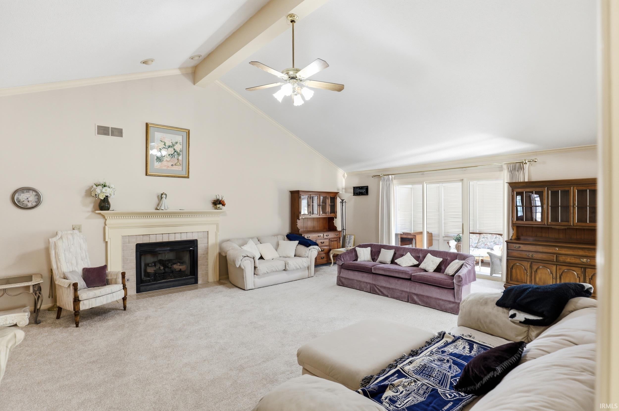 Carpeted living area featuring a tiled fireplace, a ceiling fan, and crown molding