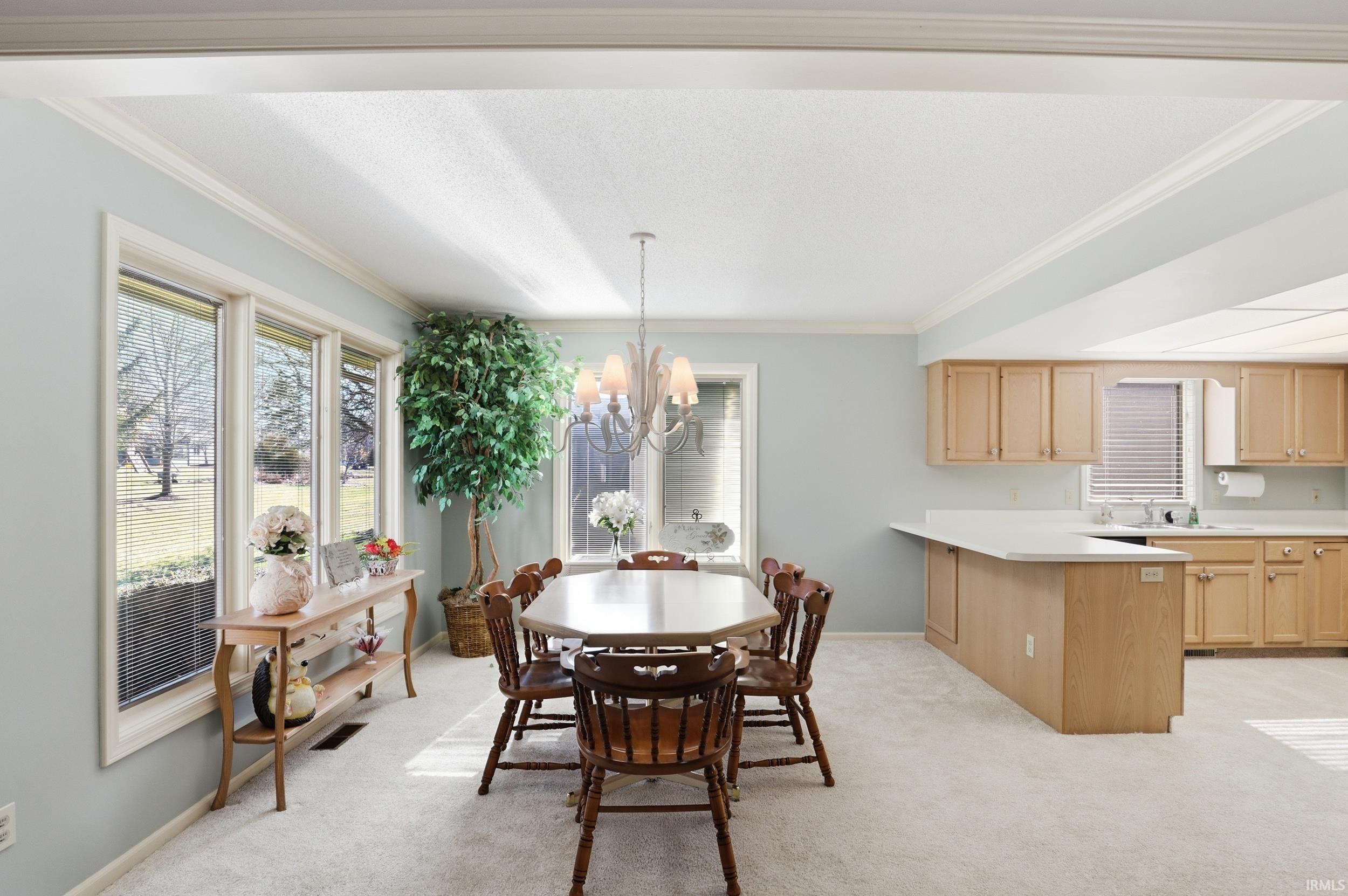 Dining area with light carpet, a chandelier, healthy amount of natural light, and ornamental molding