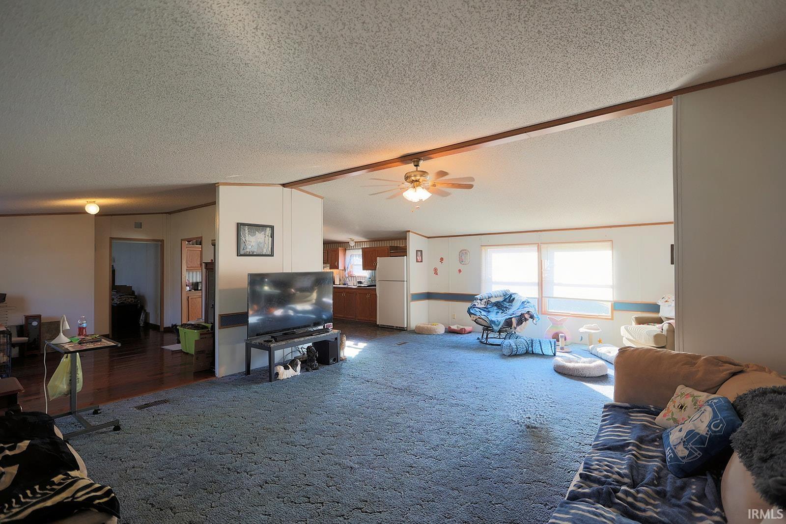 Living room featuring a ceiling fan, a textured ceiling, and beam ceiling