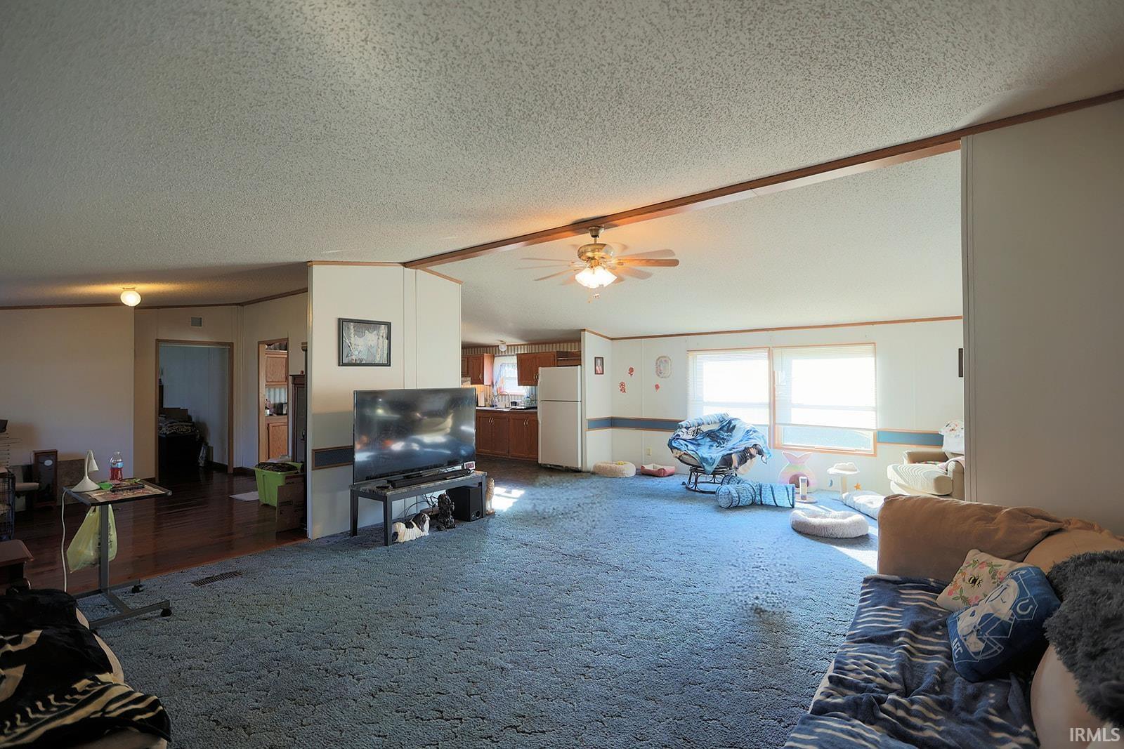 Carpeted living room with a ceiling fan, beam ceiling, and a textured ceiling