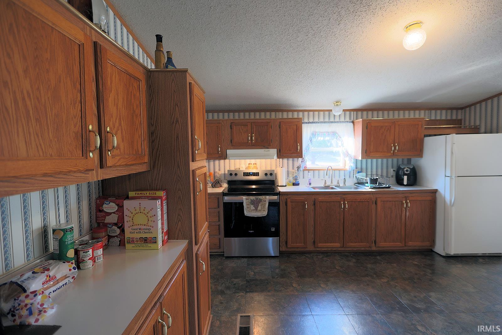 Kitchen with wallpapered walls, wood finish cabinetry, stainless steel electric stove, freestanding refrigerator, and light countertops