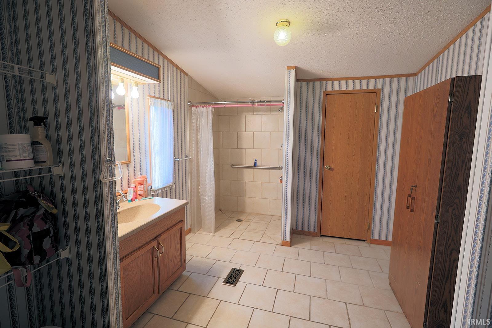 Full bathroom with wallpapered walls, a textured ceiling, vanity, a shower stall, and light tile patterned floors