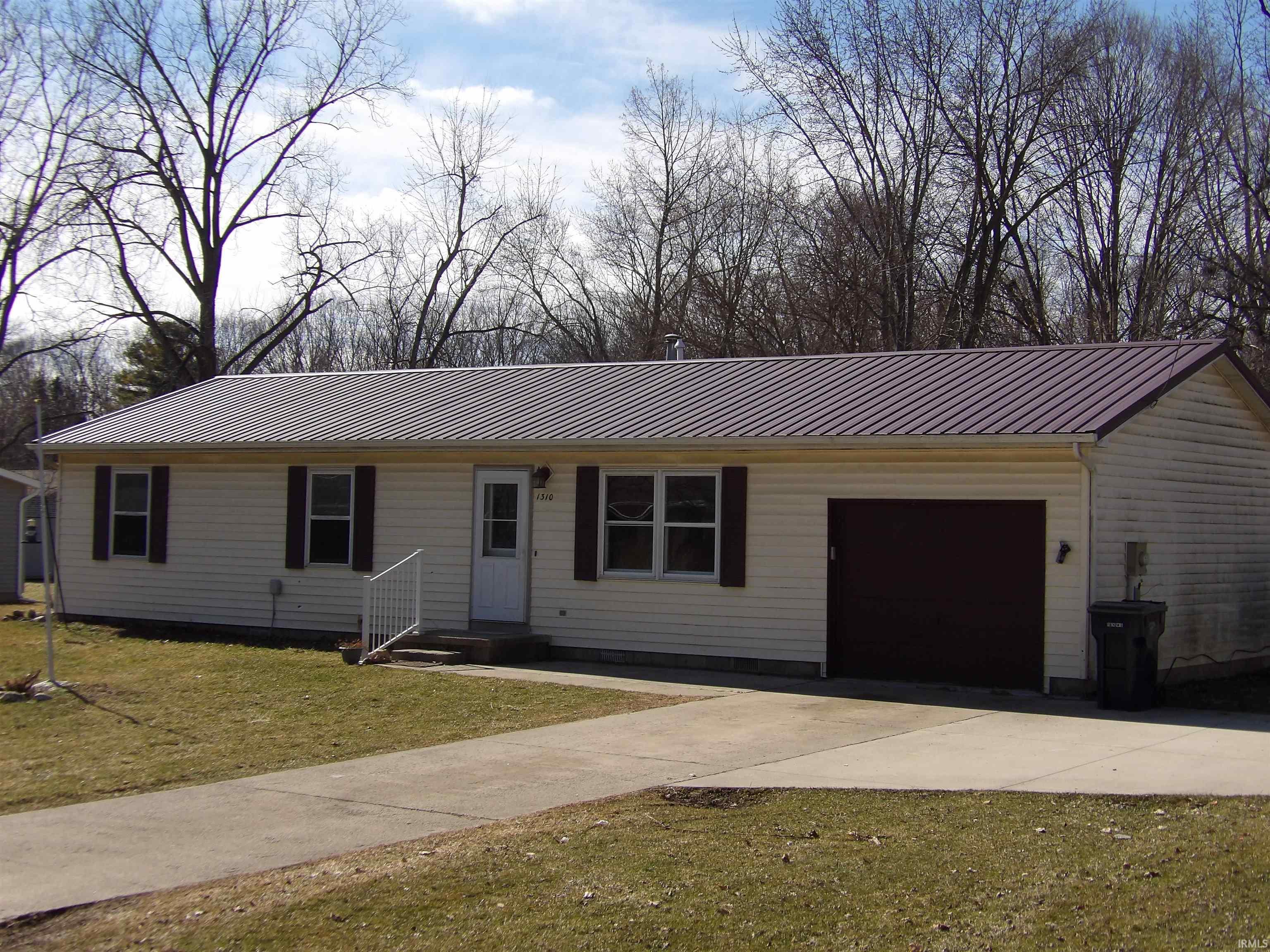 Ranch-style house with a garage, driveway, a front lawn, and a metal roof