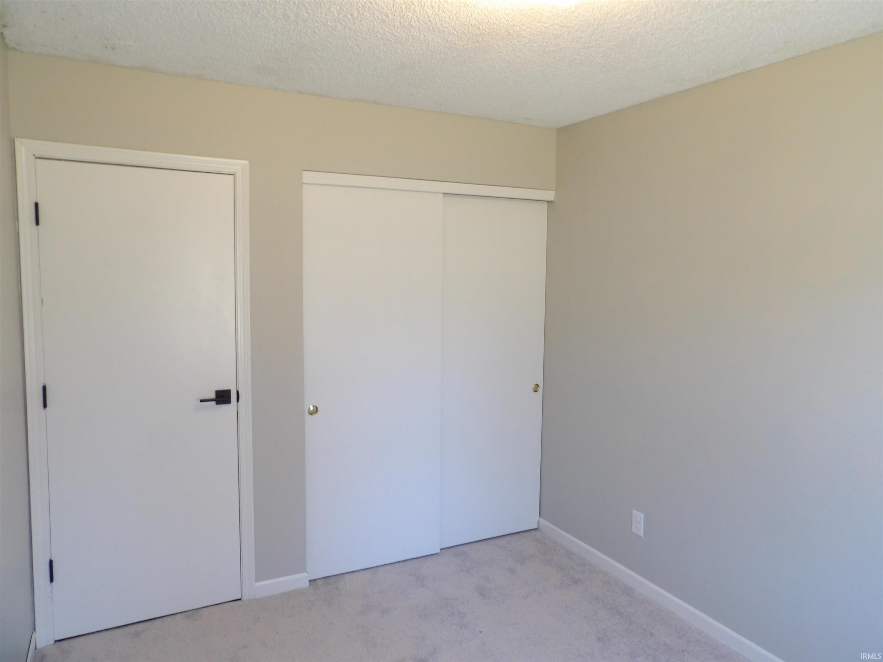 Unfurnished bedroom with light carpet, a textured ceiling, and a closet