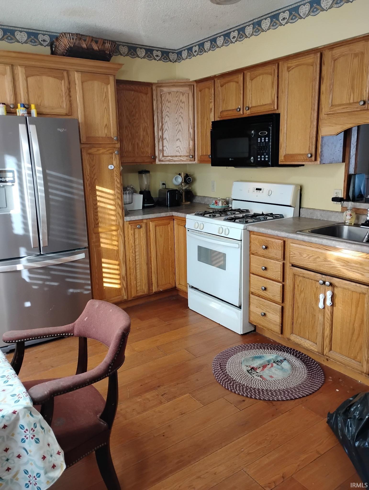 Kitchen featuring white gas range oven, stainless steel fridge, black microwave, light wood finished floors, and light countertops
