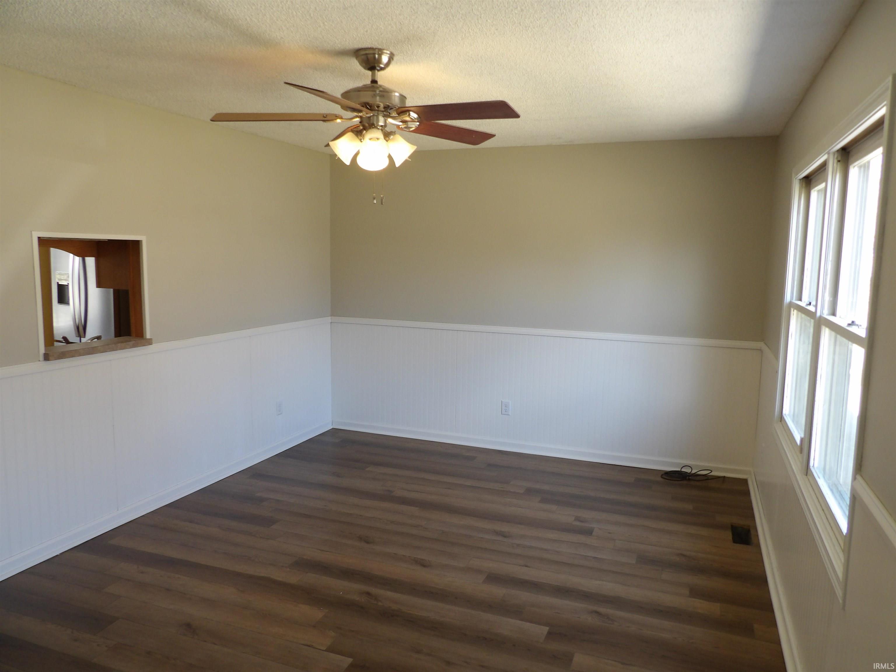Unfurnished room featuring a wainscoted wall, ceiling fan, dark wood-type flooring, and a textured ceiling
