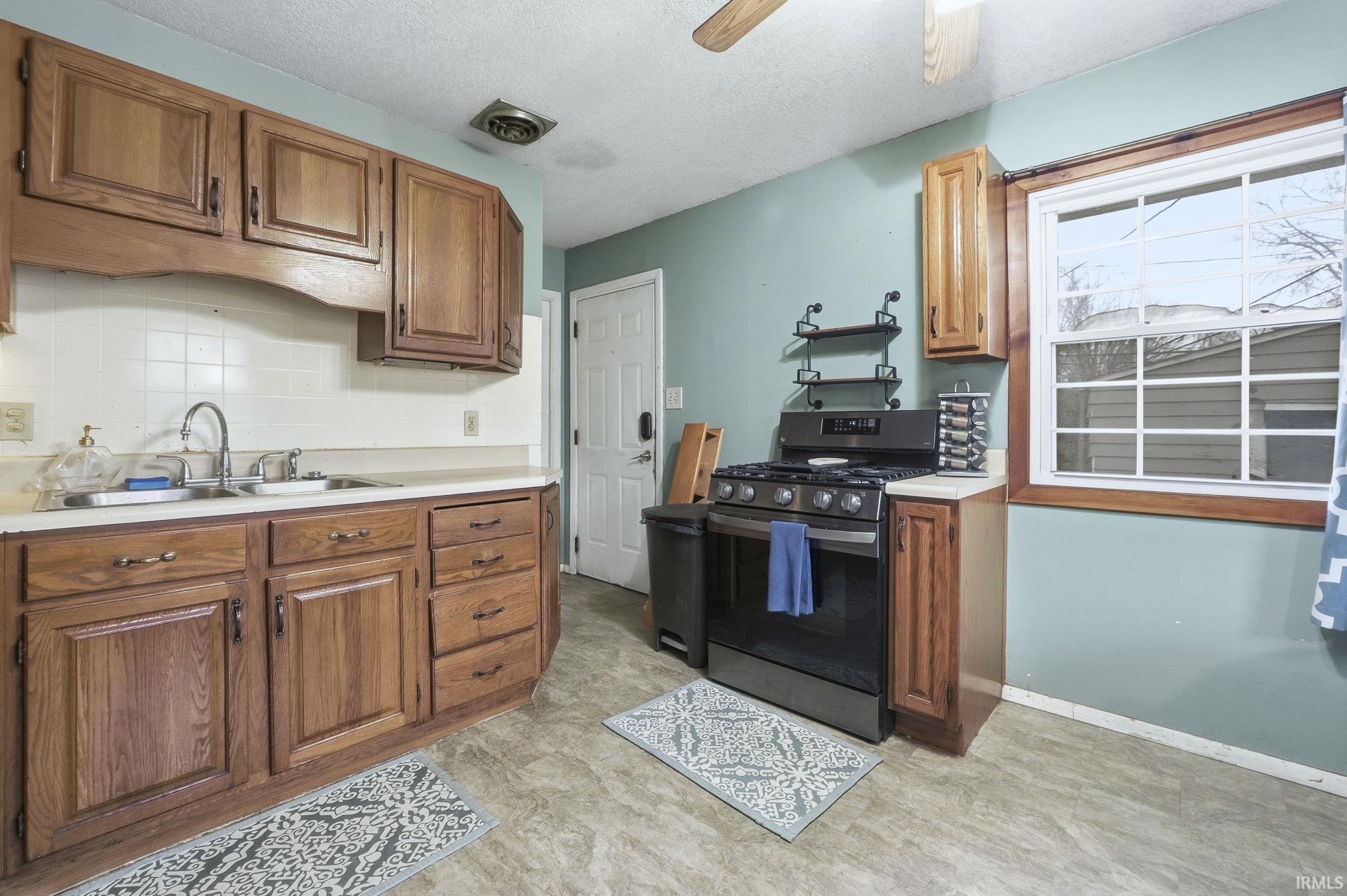 Kitchen with stainless steel gas range oven, light countertops, decorative backsplash, brown cabinets, and a textured ceiling