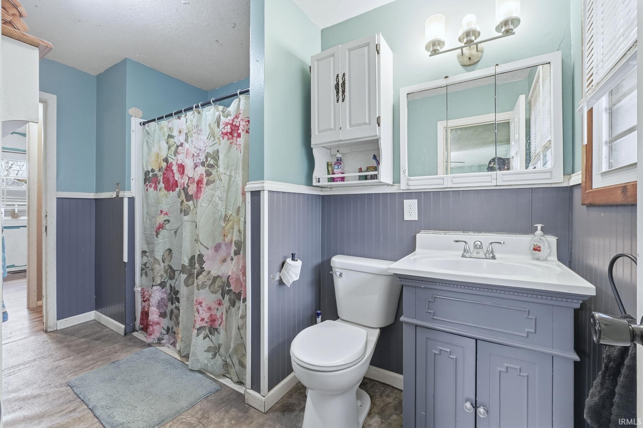 Bathroom with wainscoting, vanity, a shower stall, and light wood-style floors