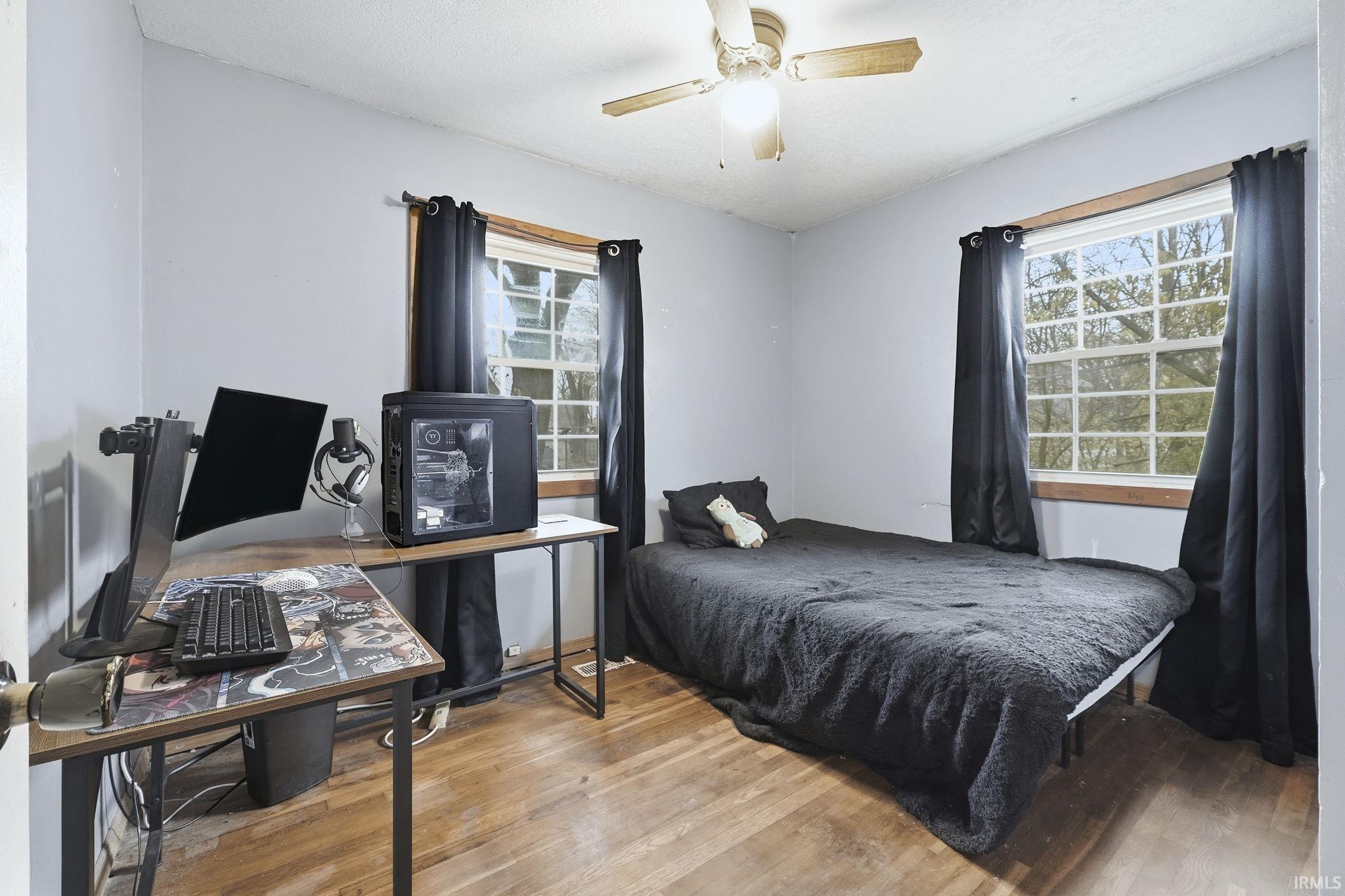 Bedroom with wood finished floors, ceiling fan, and multiple windows