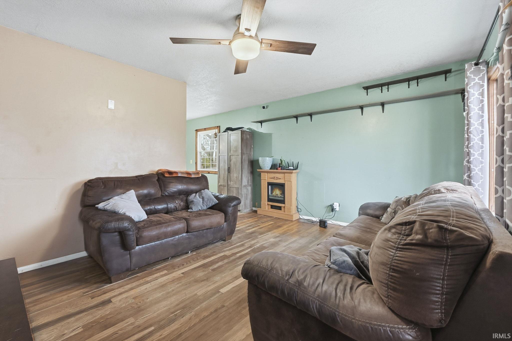Living area featuring ceiling fan, wood finished floors, and a lit fireplace