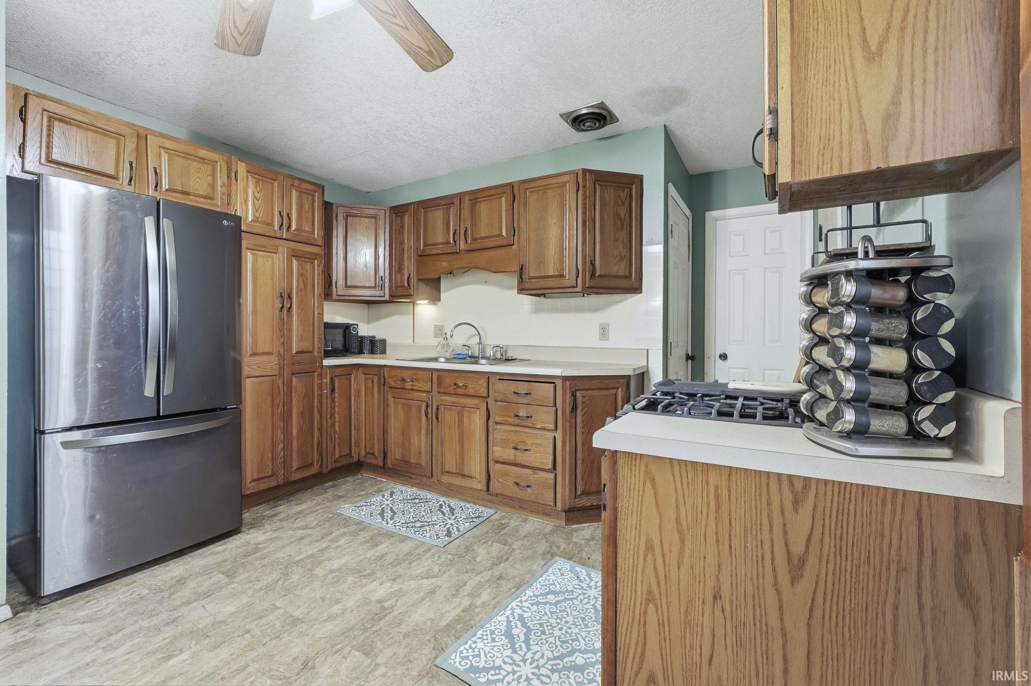 Kitchen featuring freestanding refrigerator, light countertops, brown cabinetry, a textured ceiling, and ceiling fan
