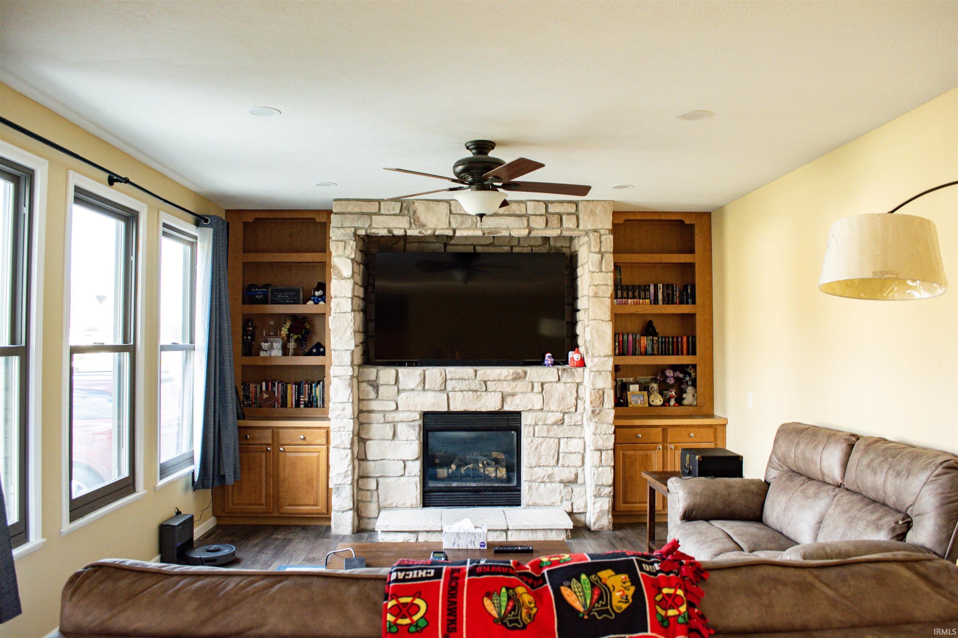 Living room featuring built in features, dark wood-style flooring, a fireplace, and a ceiling fan