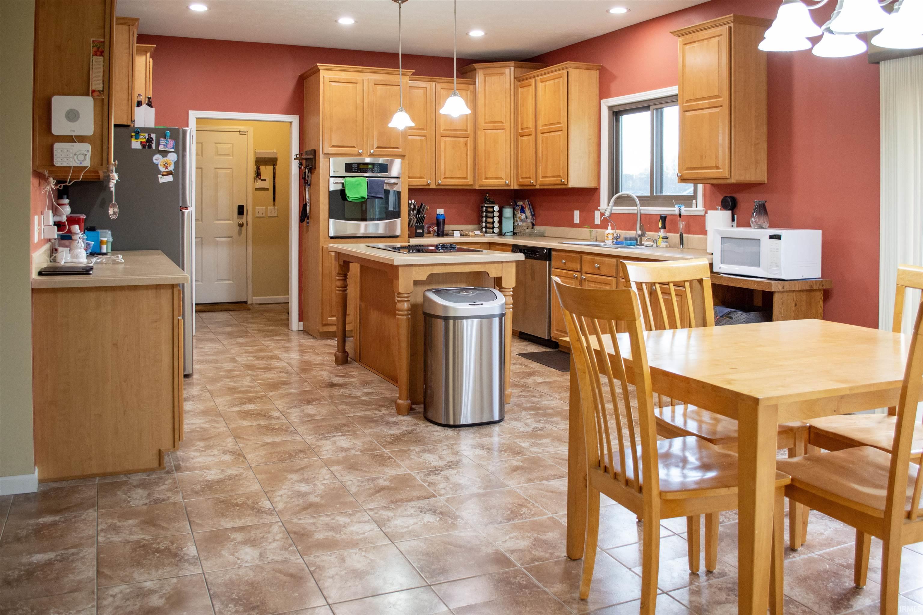 Kitchen featuring light countertops, stainless steel appliances, a center island, light wood finish cabinetry, and a chandelier