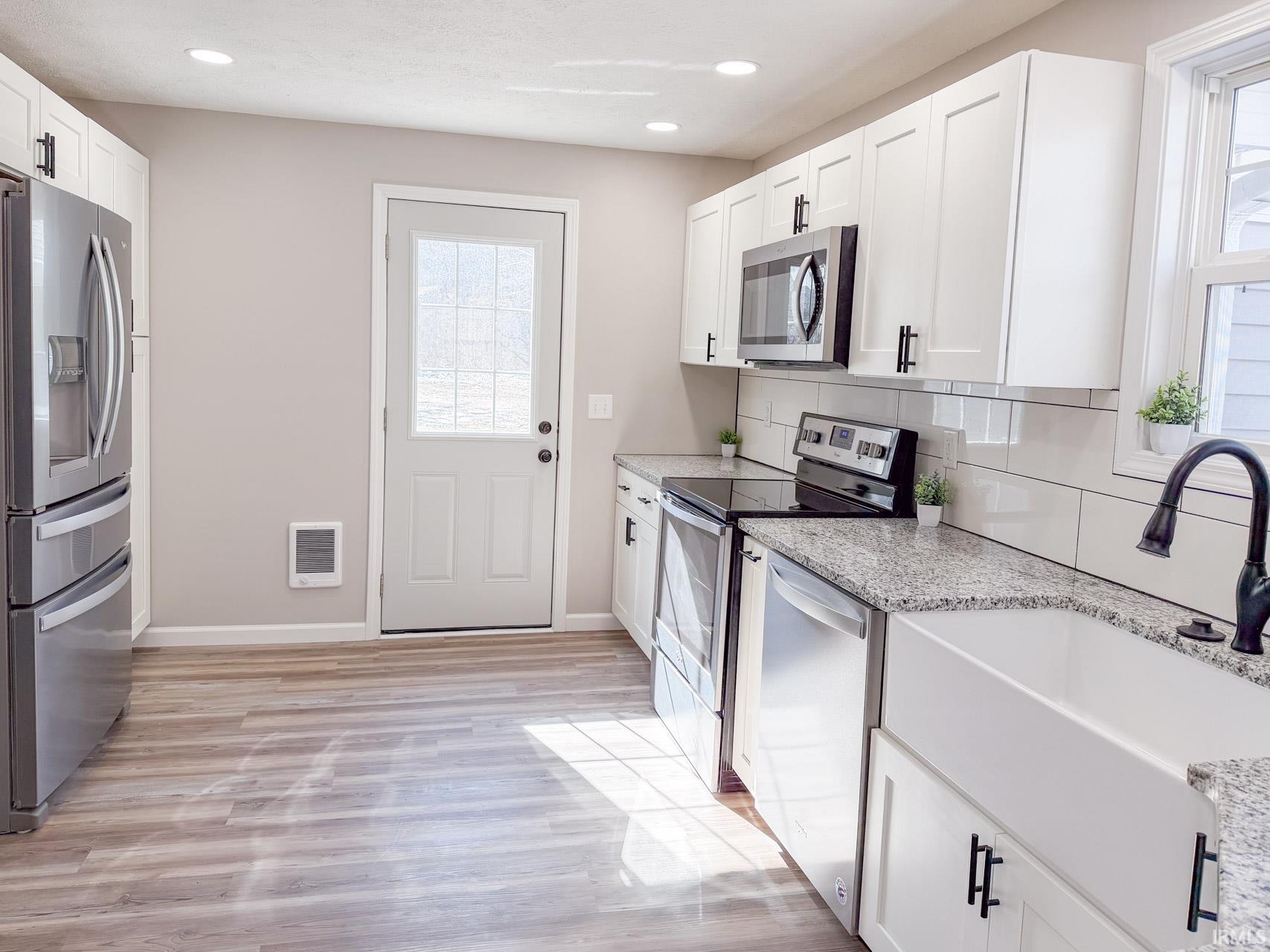 Kitchen with stainless steel appliances, white cabinetry, tasteful backsplash, light wood-style flooring, and light stone counters