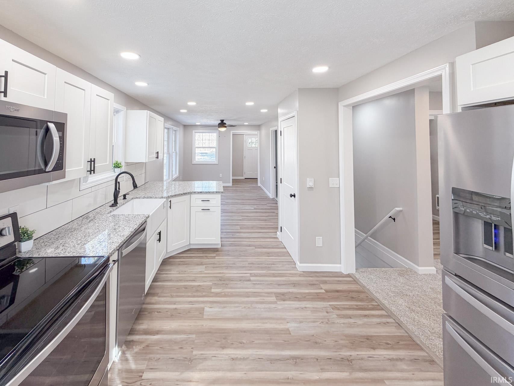 Kitchen featuring stainless steel appliances, white cabinets, light stone countertops, a peninsula, and light wood-style flooring