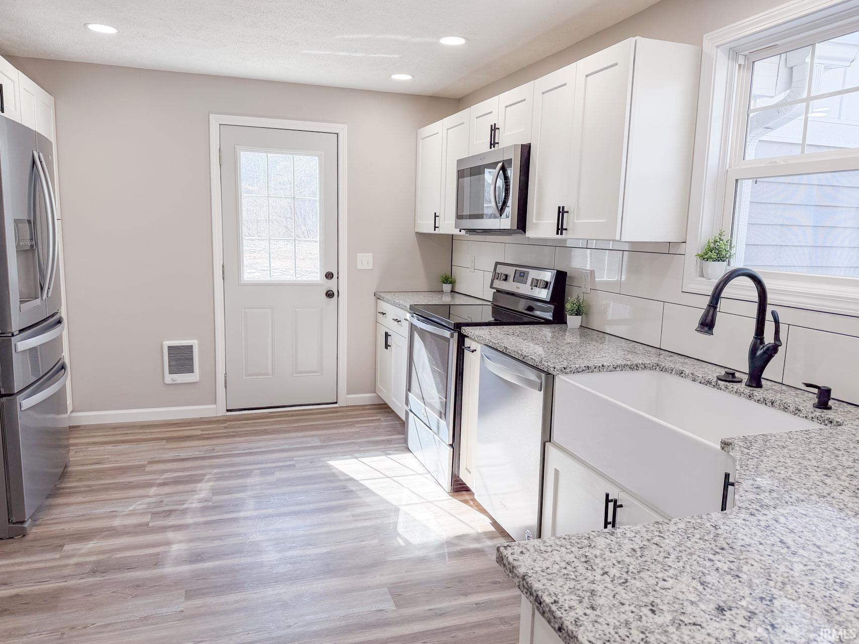 Kitchen with white cabinets, stainless steel appliances, light stone counters, backsplash, and light wood-type flooring