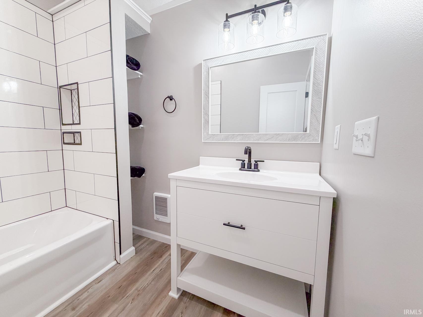 Bathroom featuring vanity, heating unit, light wood-style flooring, and tub / shower combination