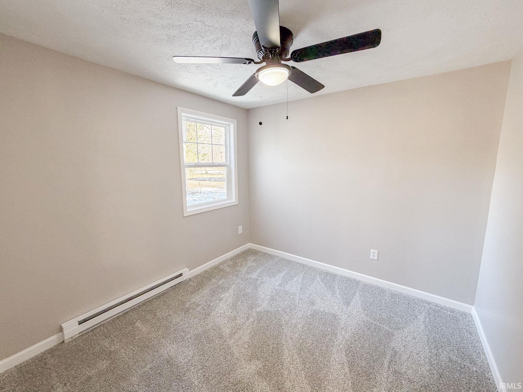 Spare room featuring a baseboard heating unit, light carpet, a ceiling fan, and a textured ceiling