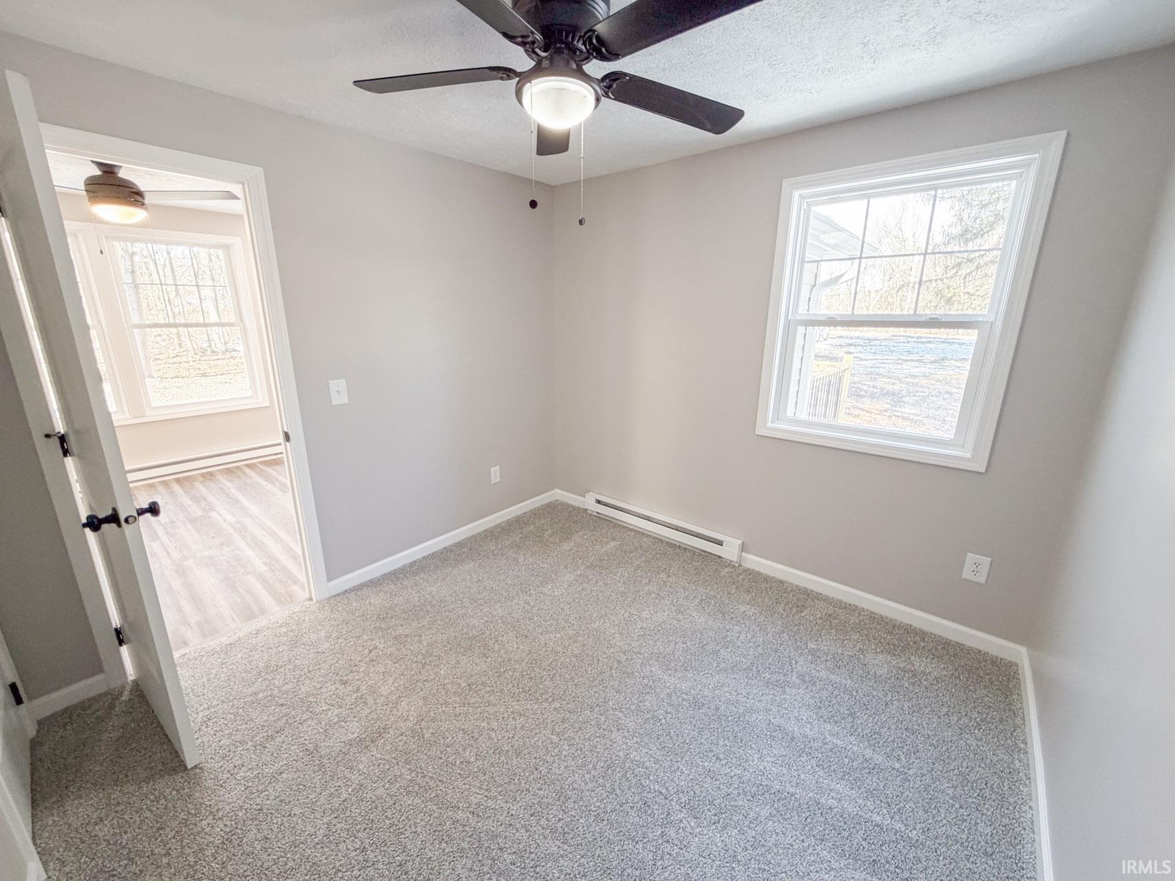 Unfurnished room featuring light carpet, baseboard heating, ceiling fan, a textured ceiling, and plenty of natural light