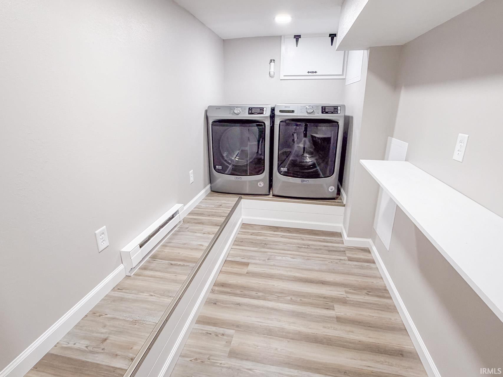 Laundry area with a baseboard radiator, washer and dryer, and light wood finished floors