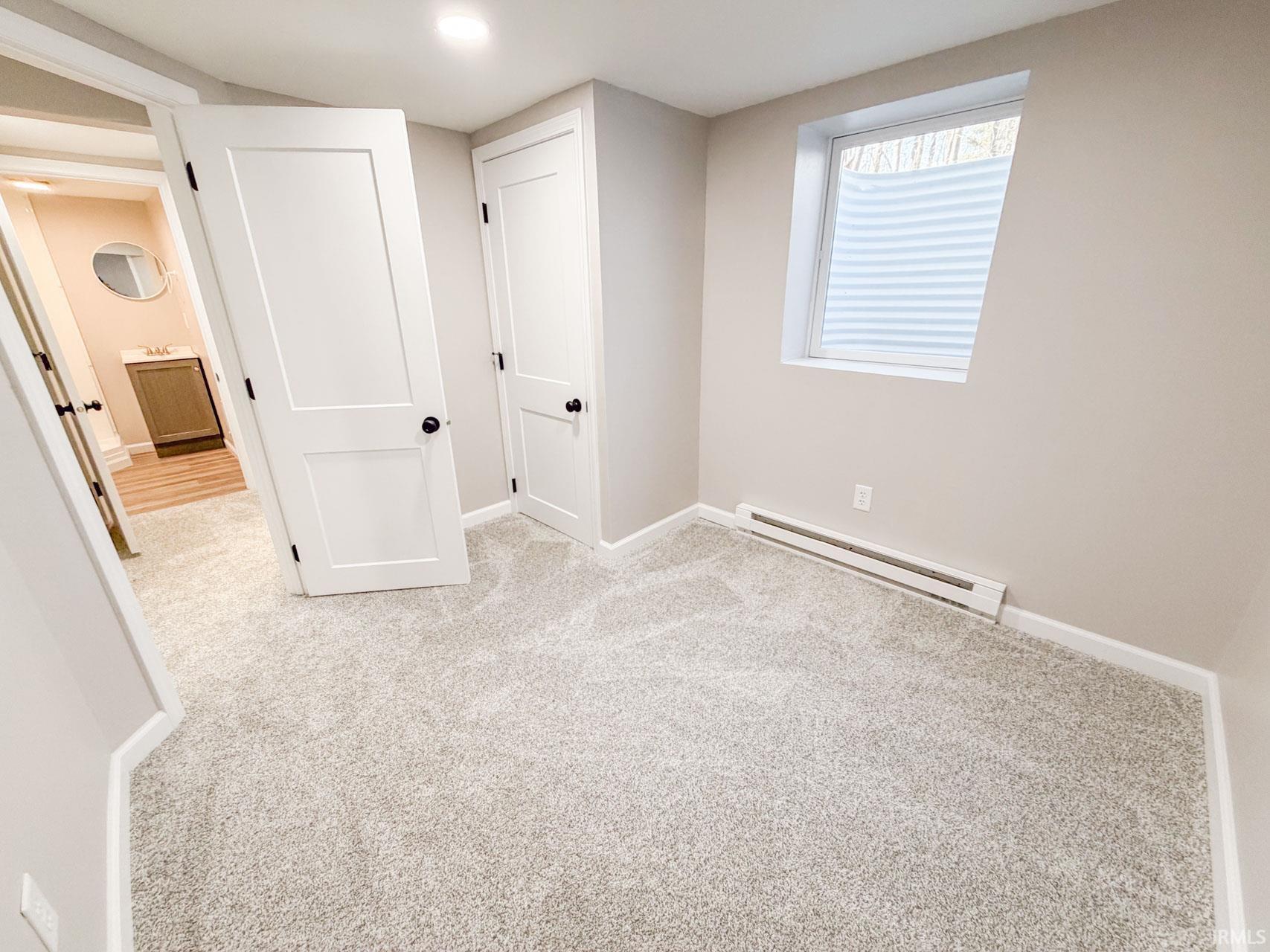 Unfurnished bedroom with light carpet and baseboard heating