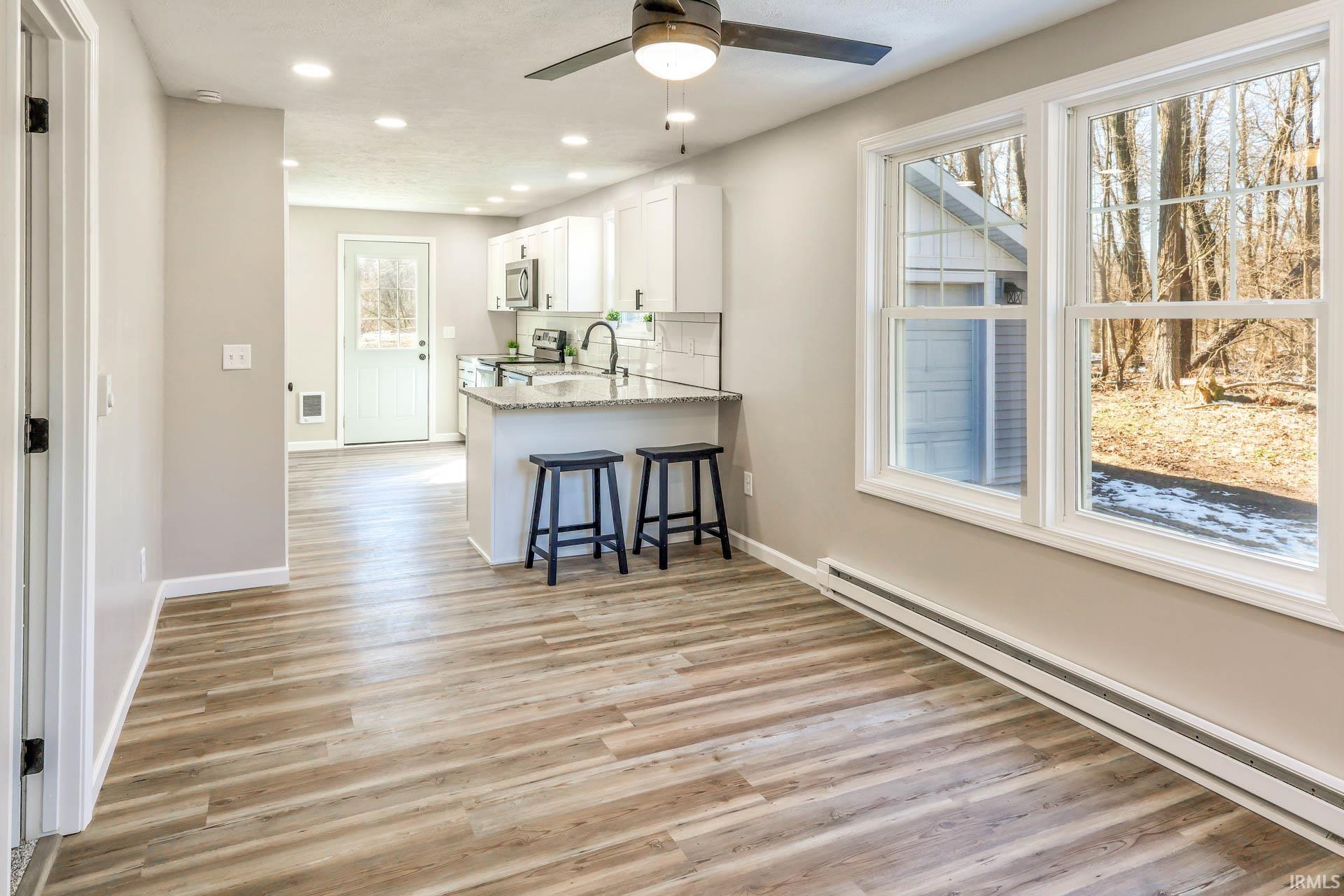 Kitchen featuring a baseboard radiator, a ceiling fan, white cabinetry, a breakfast bar area, and a peninsula