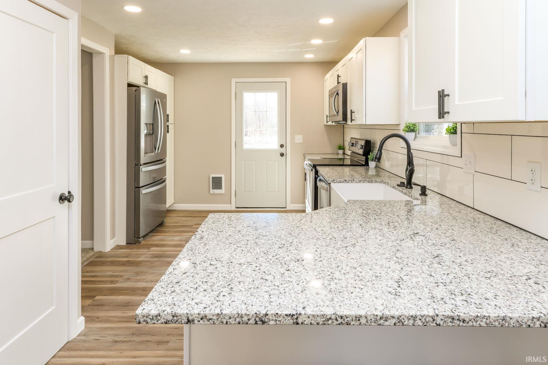 Kitchen featuring white cabinets, light stone counters, stainless steel appliances, light wood finished floors, and recessed lighting