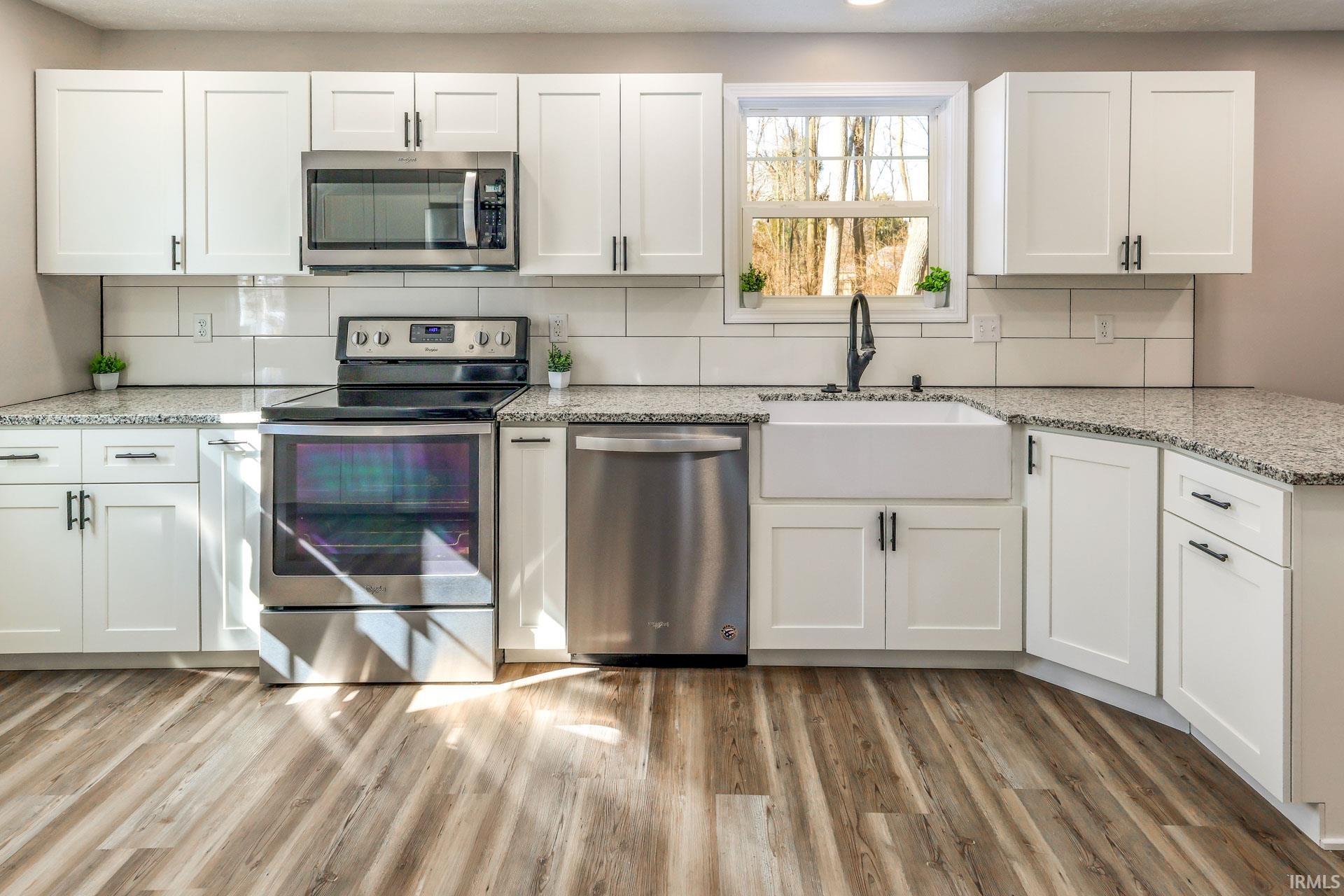 Kitchen featuring stainless steel appliances, light stone countertops, white cabinetry, and light wood-style flooring