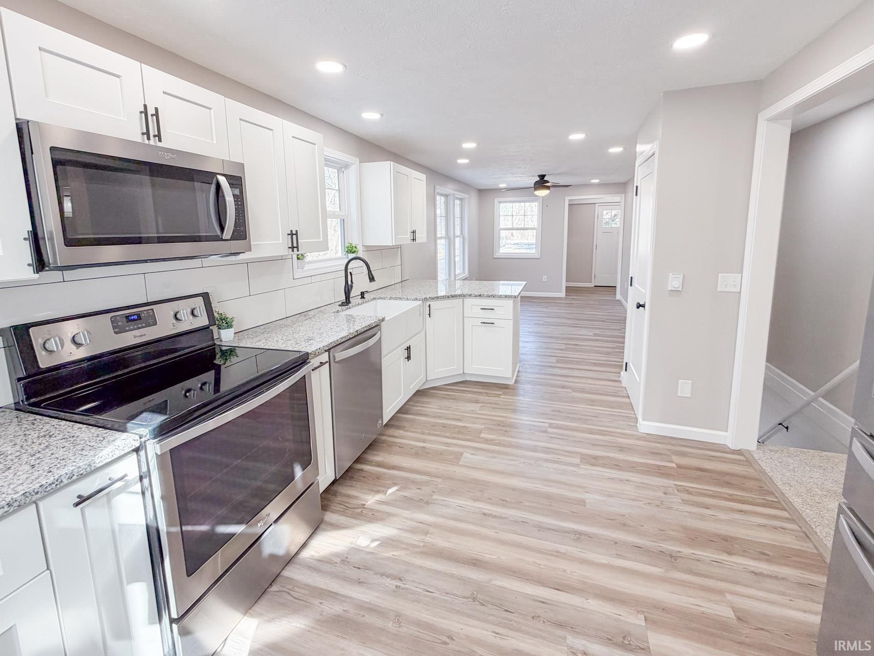 Kitchen with stainless steel appliances, white cabinets, light wood finished floors, light stone counters, and recessed lighting
