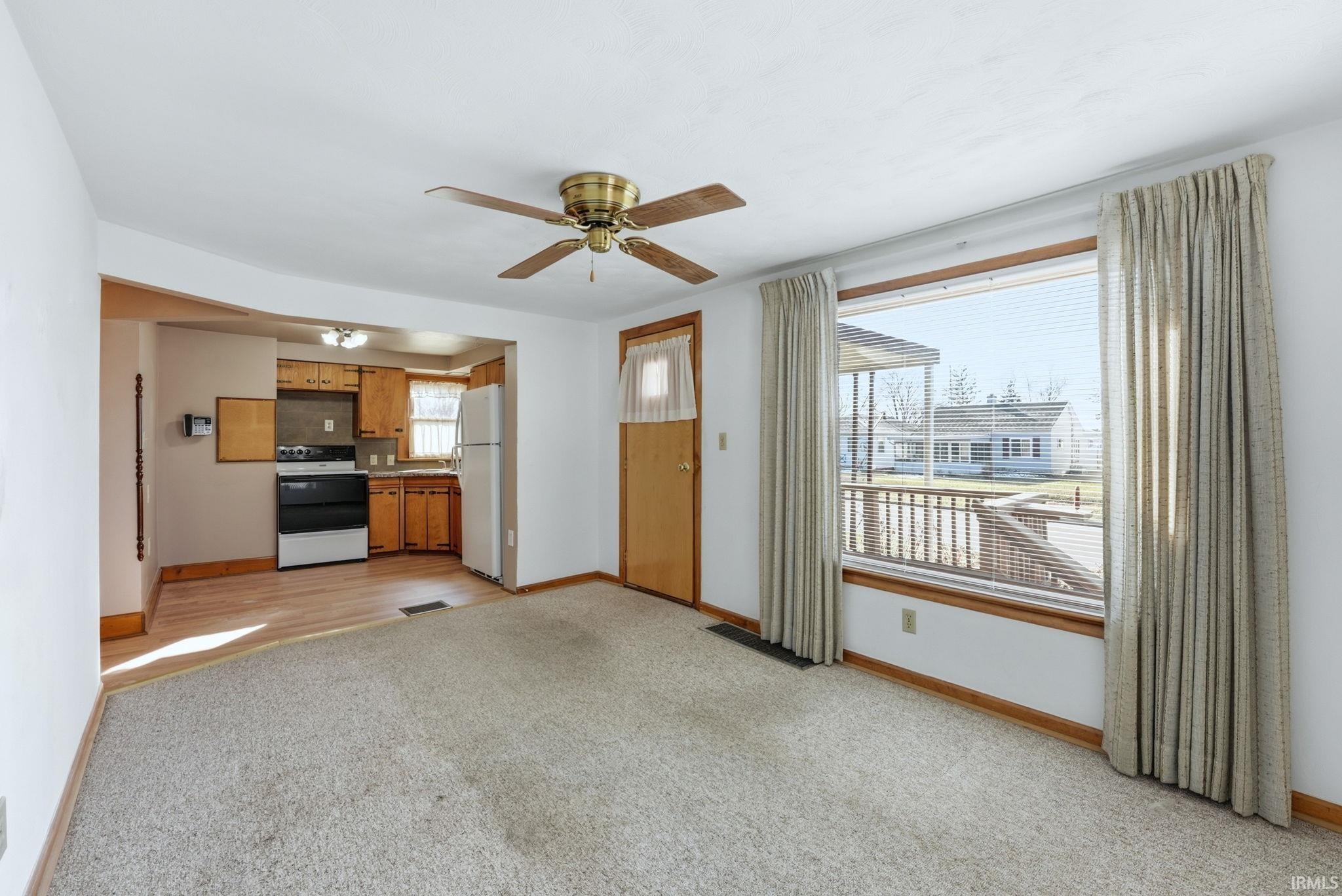 Kitchen with wood finish cabinetry, white appliances, light carpet, a ceiling fan, and light countertops