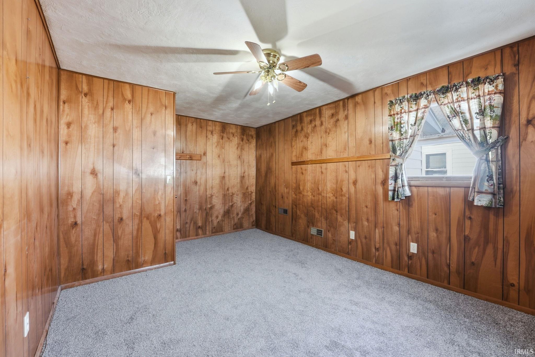 Carpeted empty room featuring a ceiling fan and wood walls