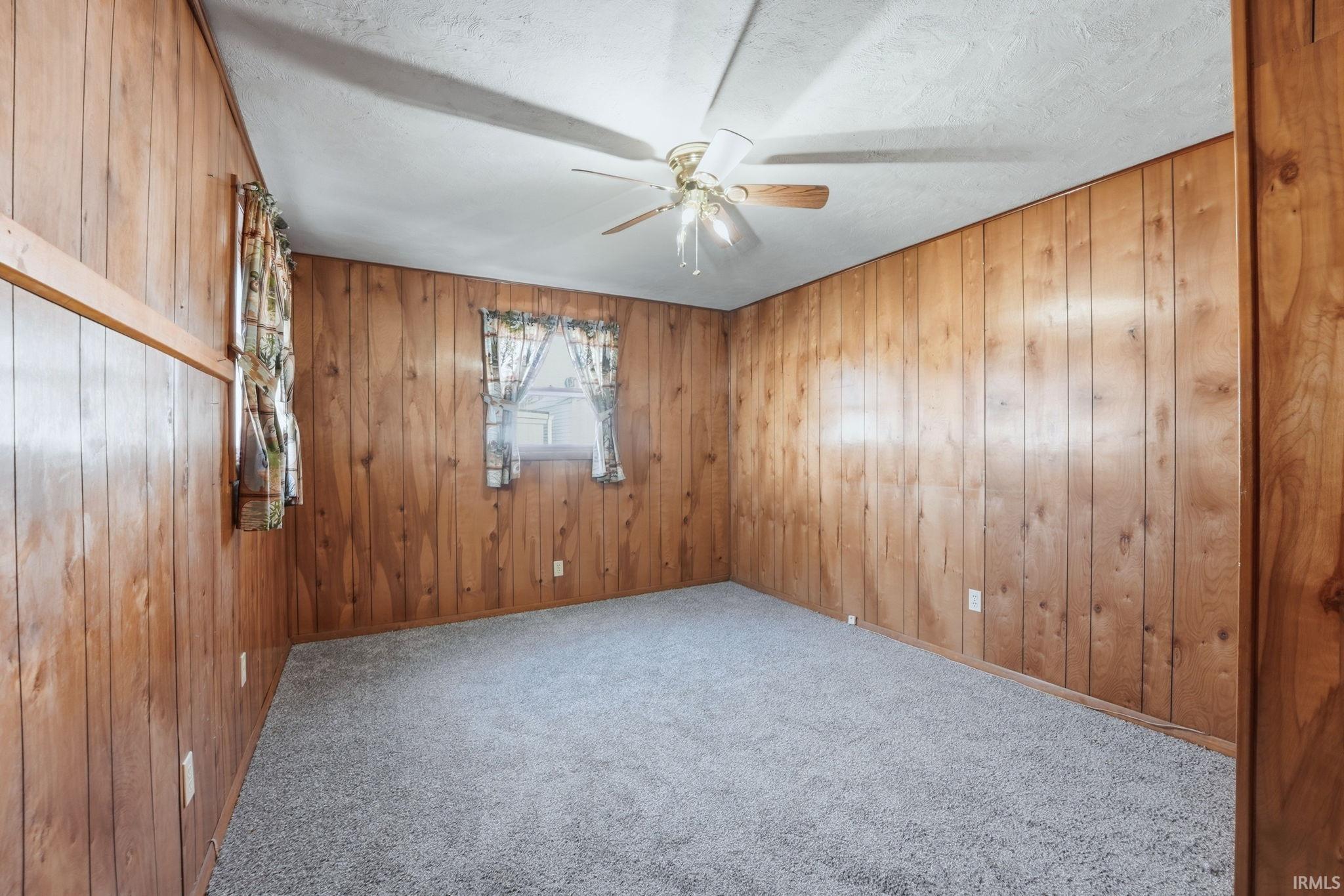 Carpeted spare room featuring wooden walls, ceiling fan, and a textured ceiling
