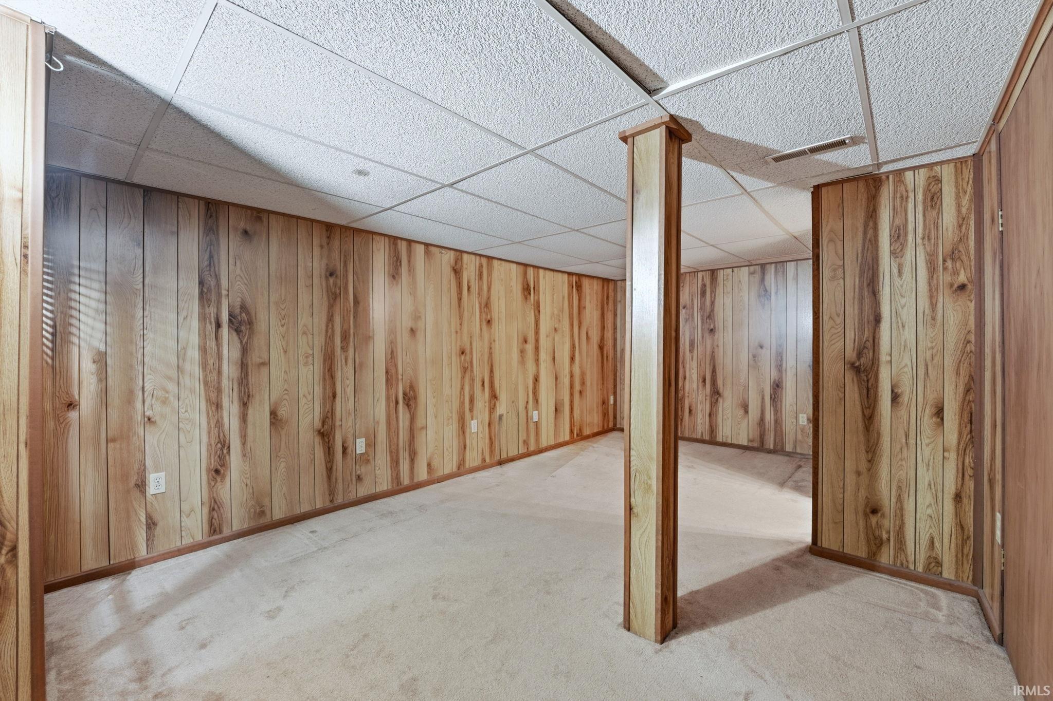 Finished basement with a paneled ceiling, light colored carpet, and wooden walls